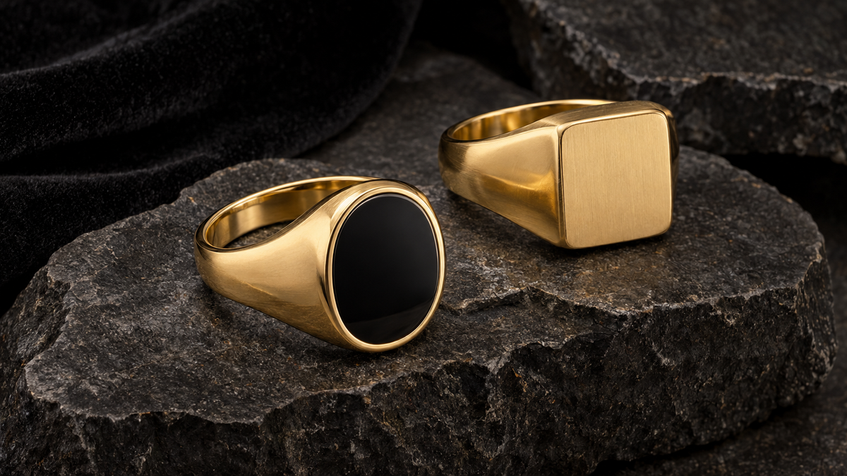 Illustrative gold-tone signet-style rings, one with a dark stone, on grey rock; not verified depictions of listed products, metal purity or stone identity.