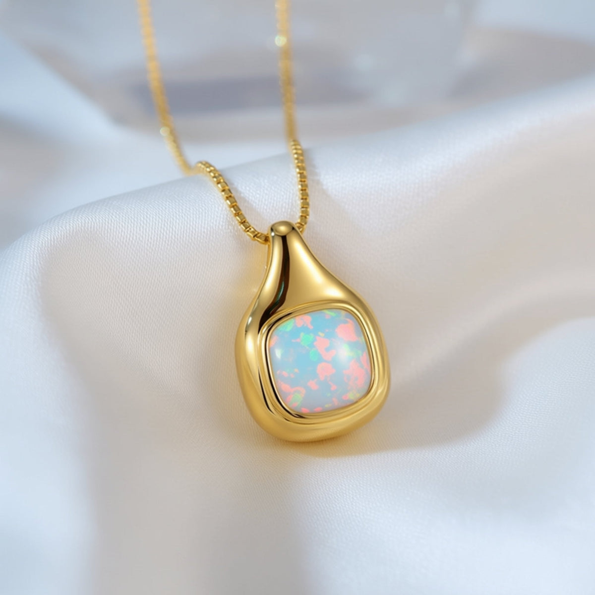Gold-toned teardrop pendant necklace with an iridescent pink and blue stone resting on white fabric.