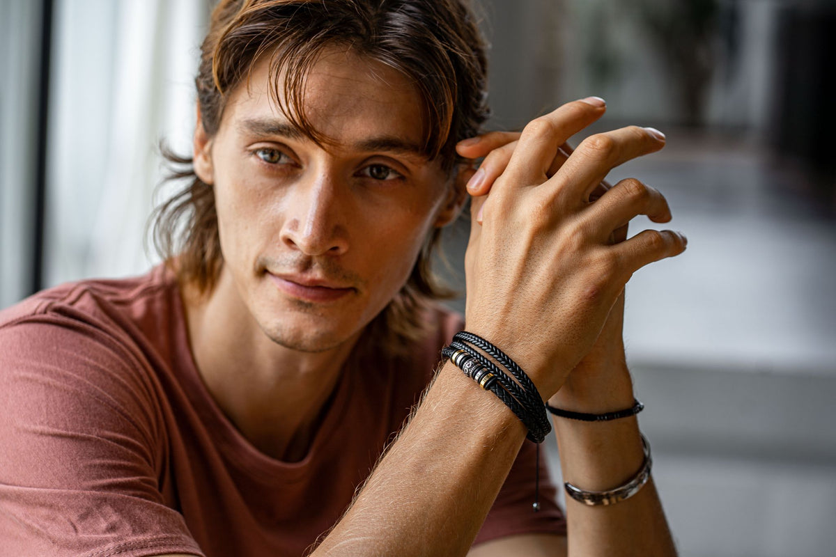 Close-up of a young man resting his hands, wearing braided black bracelets with metal beads and a silver-toned cuff.