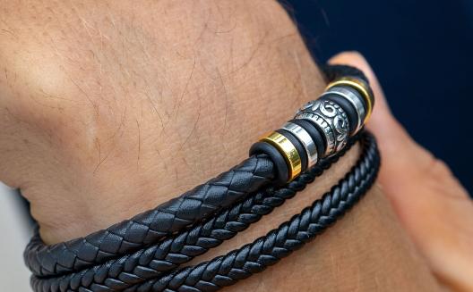 Close-up of a wrist wearing several black braided leather bracelets with gold-toned rings and an ornate silver-toned bead.