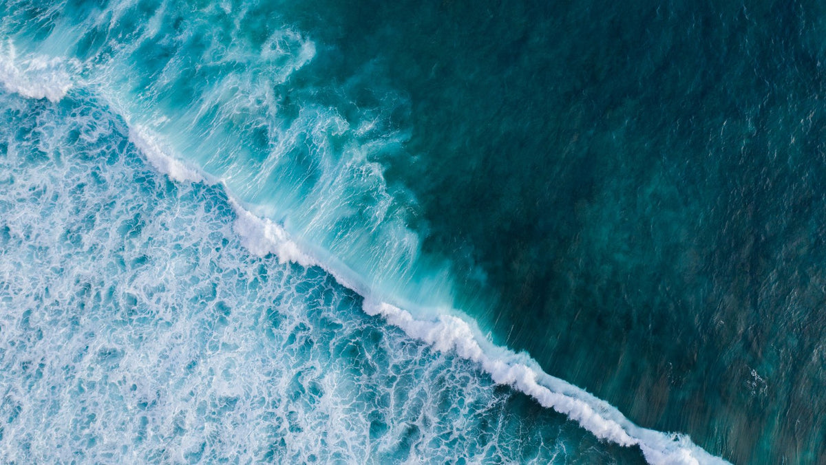 Aerial top-down view of a turquoise ocean wave breaking diagonally into white foam.