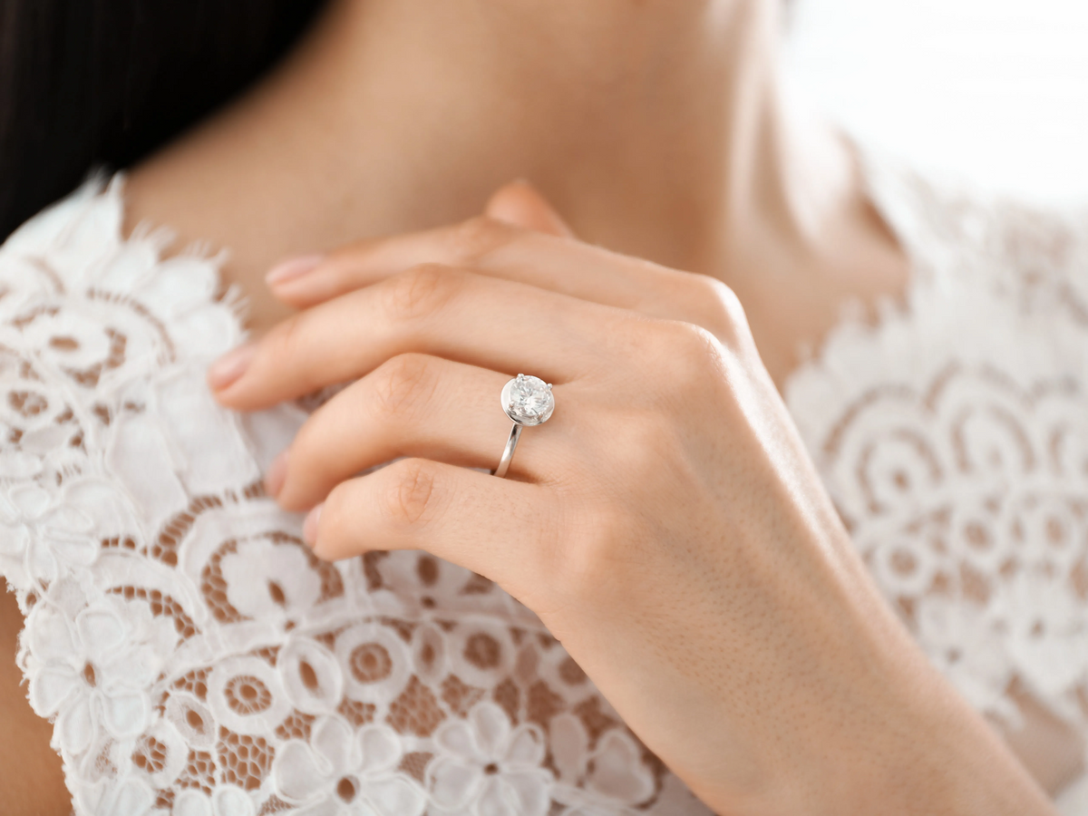 Close-up of a hand resting on a lace top, wearing a silver-toned ring with a round clear centerpiece.