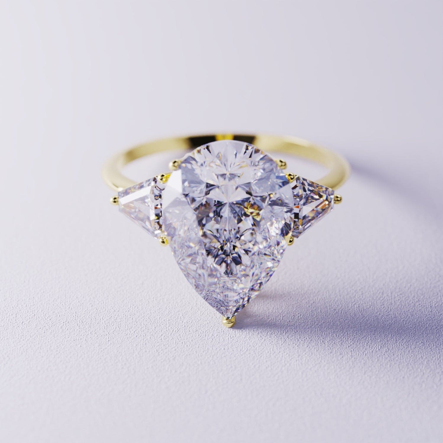 Gold-toned ring with a large pear-shaped clear gemstone and two triangular side stones on a pale purple background.