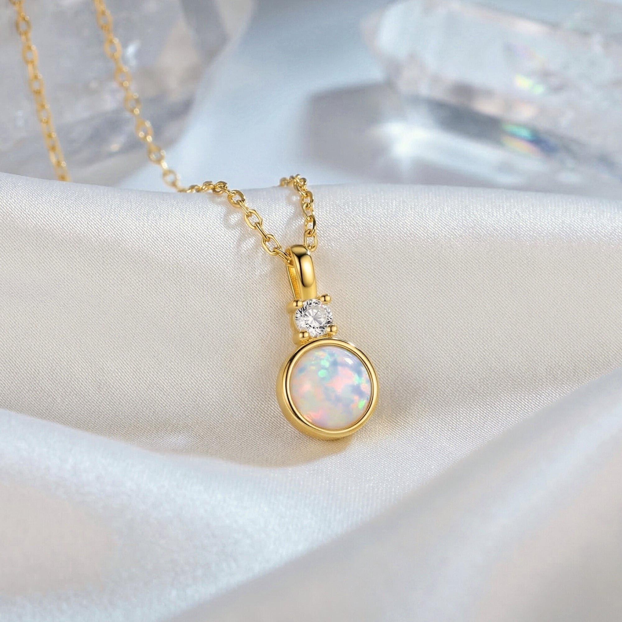 Yellow gold round white opal pendant necklace with a clear accent stone on white silk with crystals.