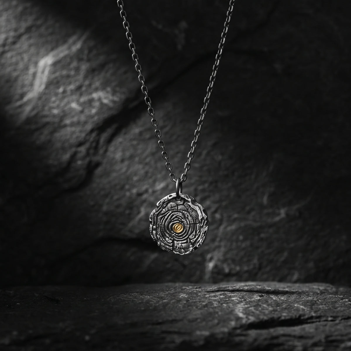 Front view of the silver growth ring pendant with a gold accent suspended over dark stone.