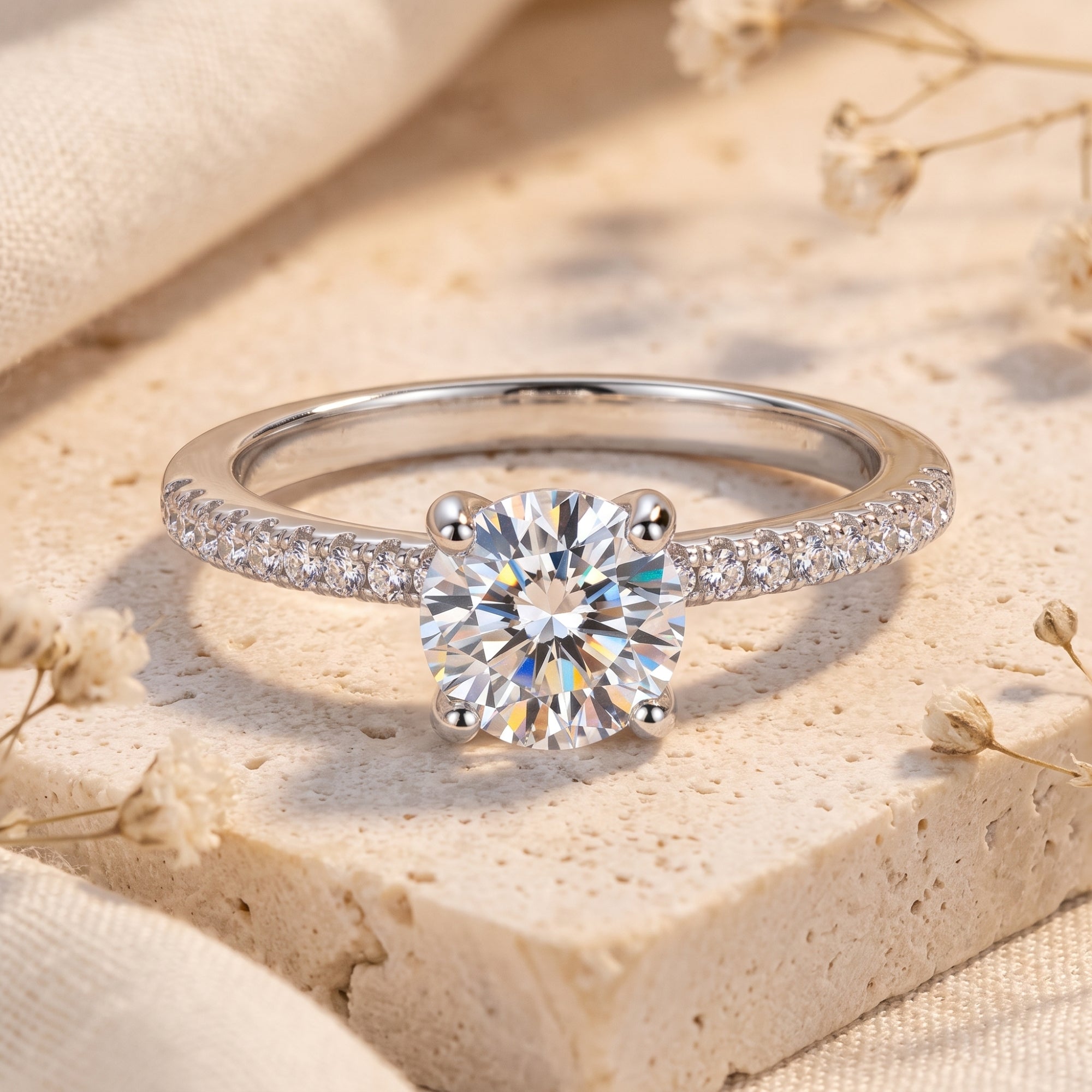 Front close-up of a silver ring with a round clear center stone in a four-prong setting and pavé shoulder accents.