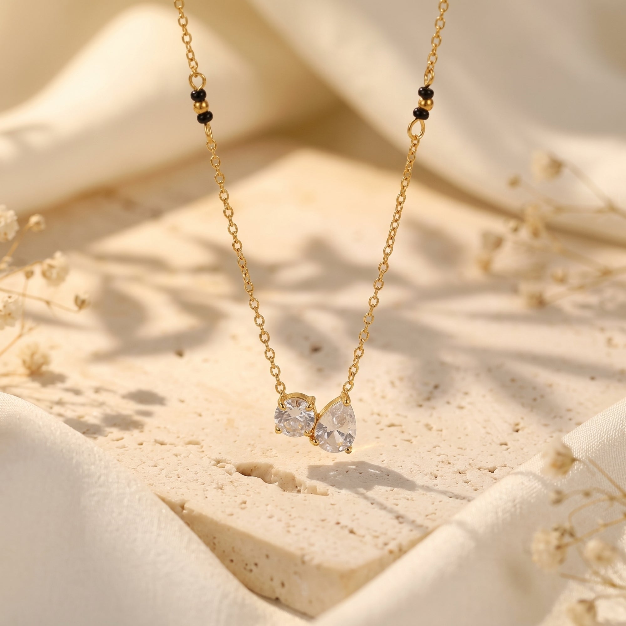Close-up of a gold-tone chain necklace featuring round and pear-cut clear stone pendants with black bead accents.