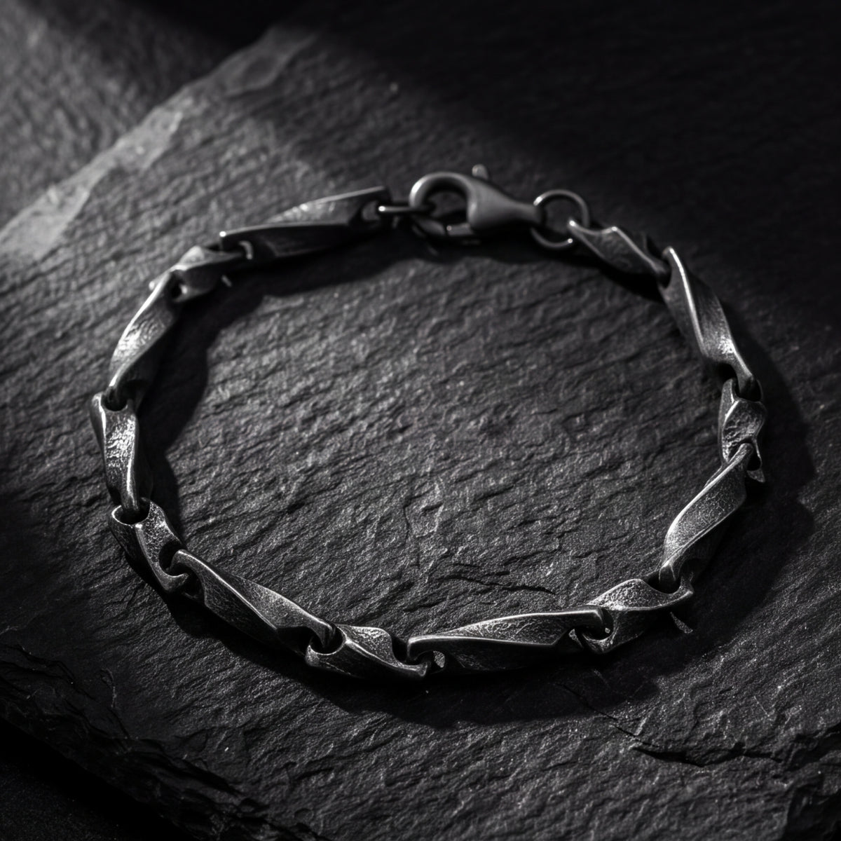 Close-up of a dark oxidized silver twisted-link bracelet arranged in a circle on black slate.