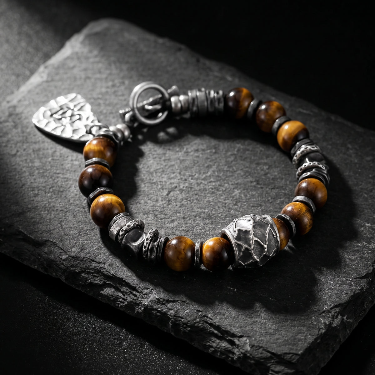 The Artisan Beaded Bracelet with brown tiger's eye beads and carved silver spacers rests on a black stone slab.