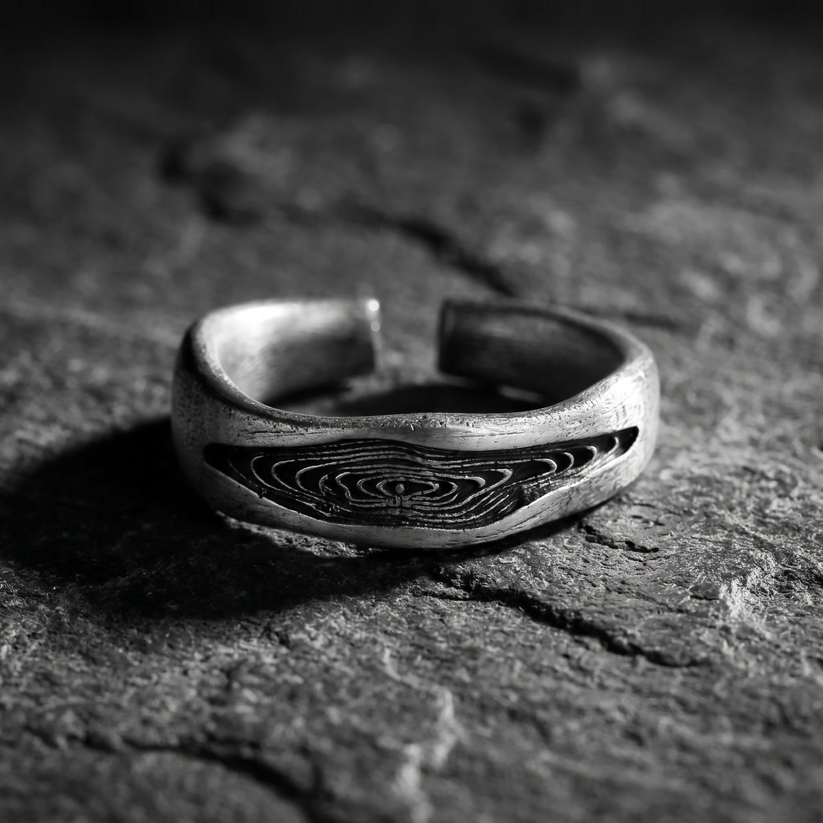 Silver open band ring with carved wood grain detailing, resting on a textured dark slate surface.