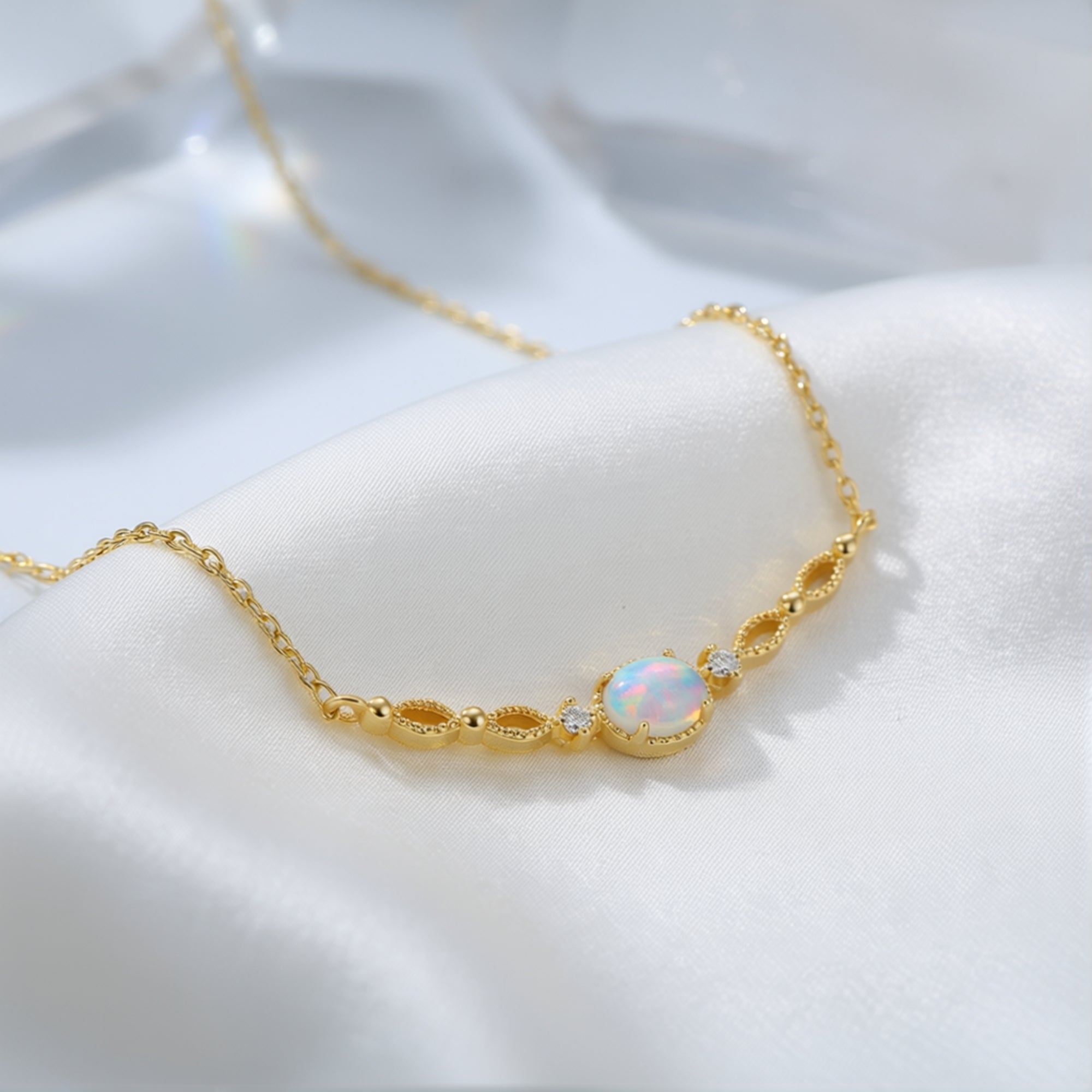 Gold-tone sterling silver necklace with an oval white opal pendant resting on white silk fabric.