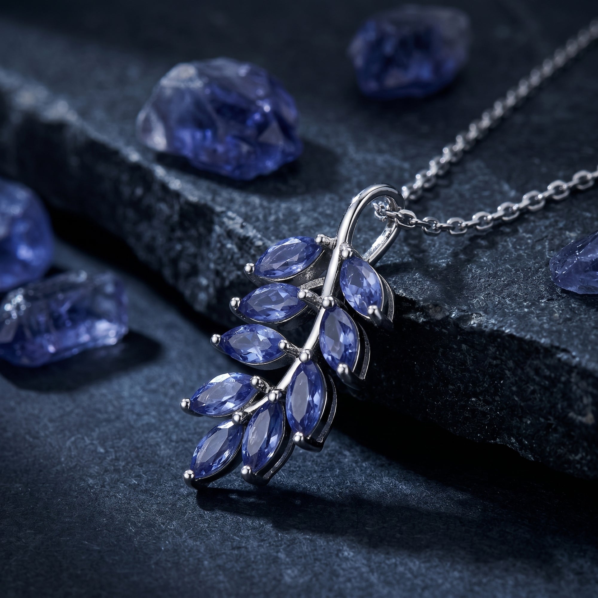 Macro view of marquise tanzanite stones in a white gold cluster pendant setting on a dark stone surface.
