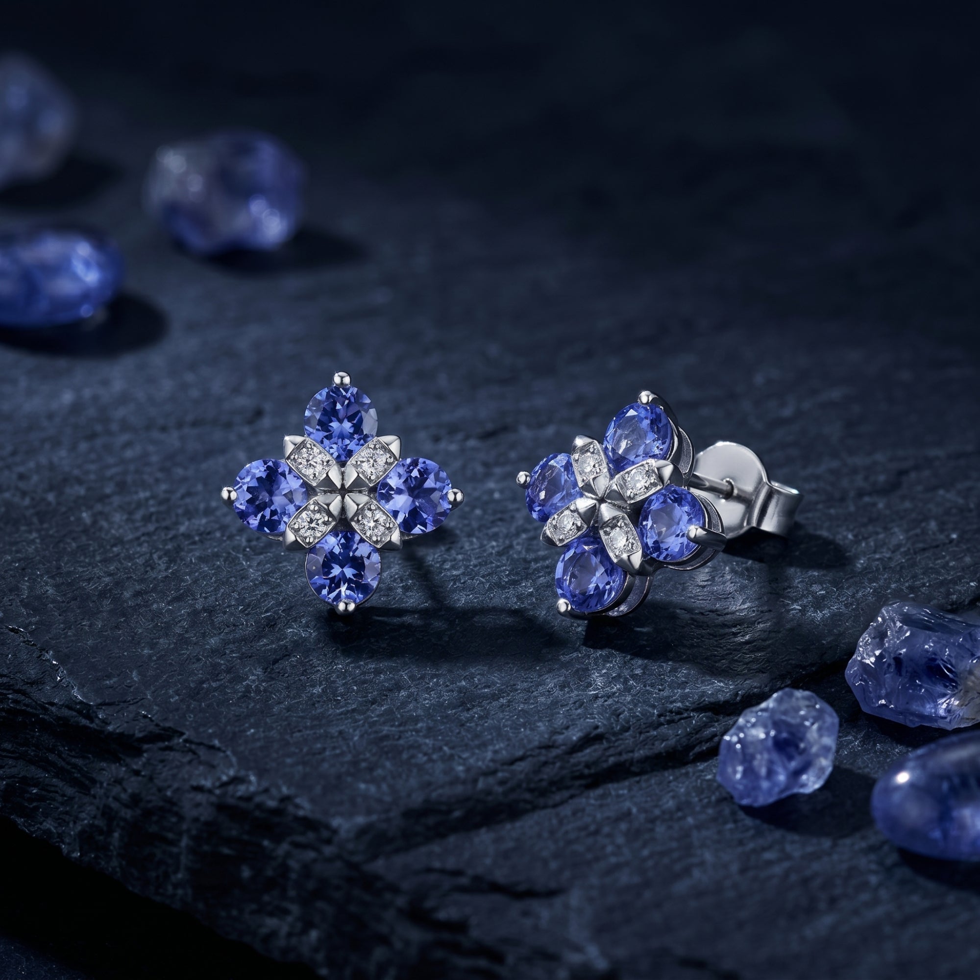 Silver flower cluster earrings with round tanzanite stones on a dark stone surface with raw gems.