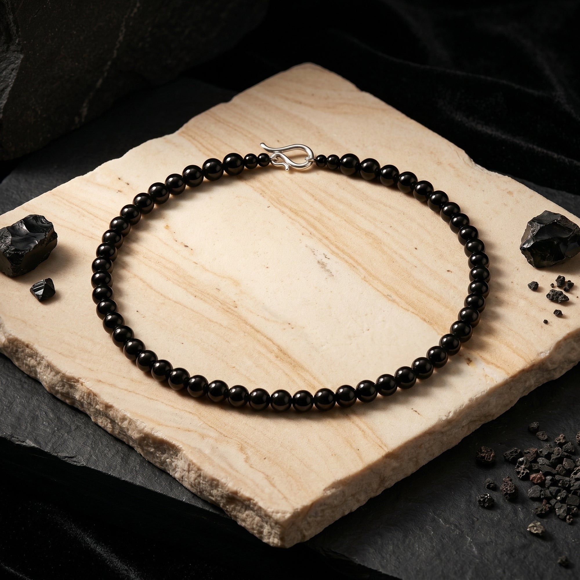 6mm round black onyx beaded necklace with a sterling silver S-hook clasp, styled on a tan stone slab.