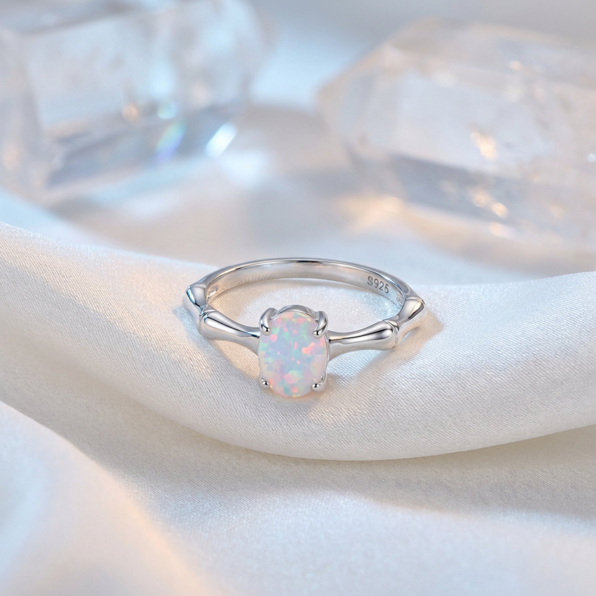 Oval-cut natural opal ring in S925 sterling silver with a bamboo-style band, resting on white silk fabric.