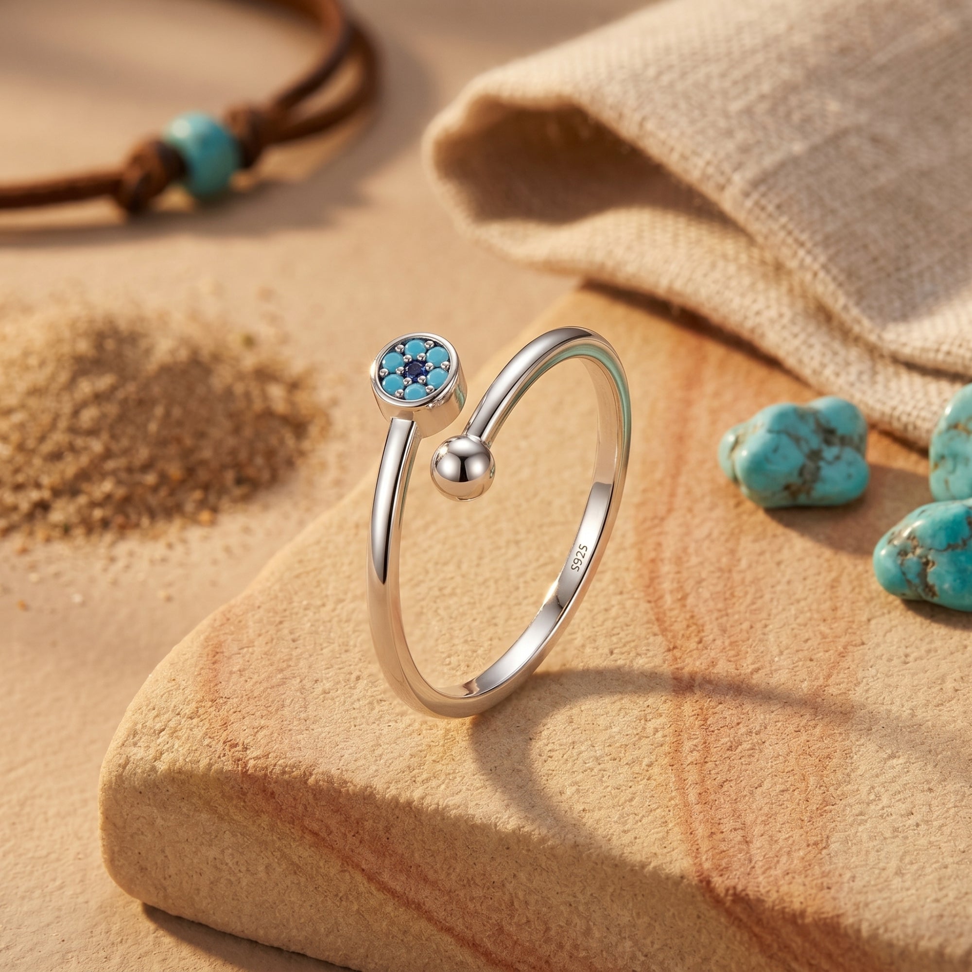 Silver bypass ring with a turquoise cabochon and polished sphere on a desert-themed stone background.