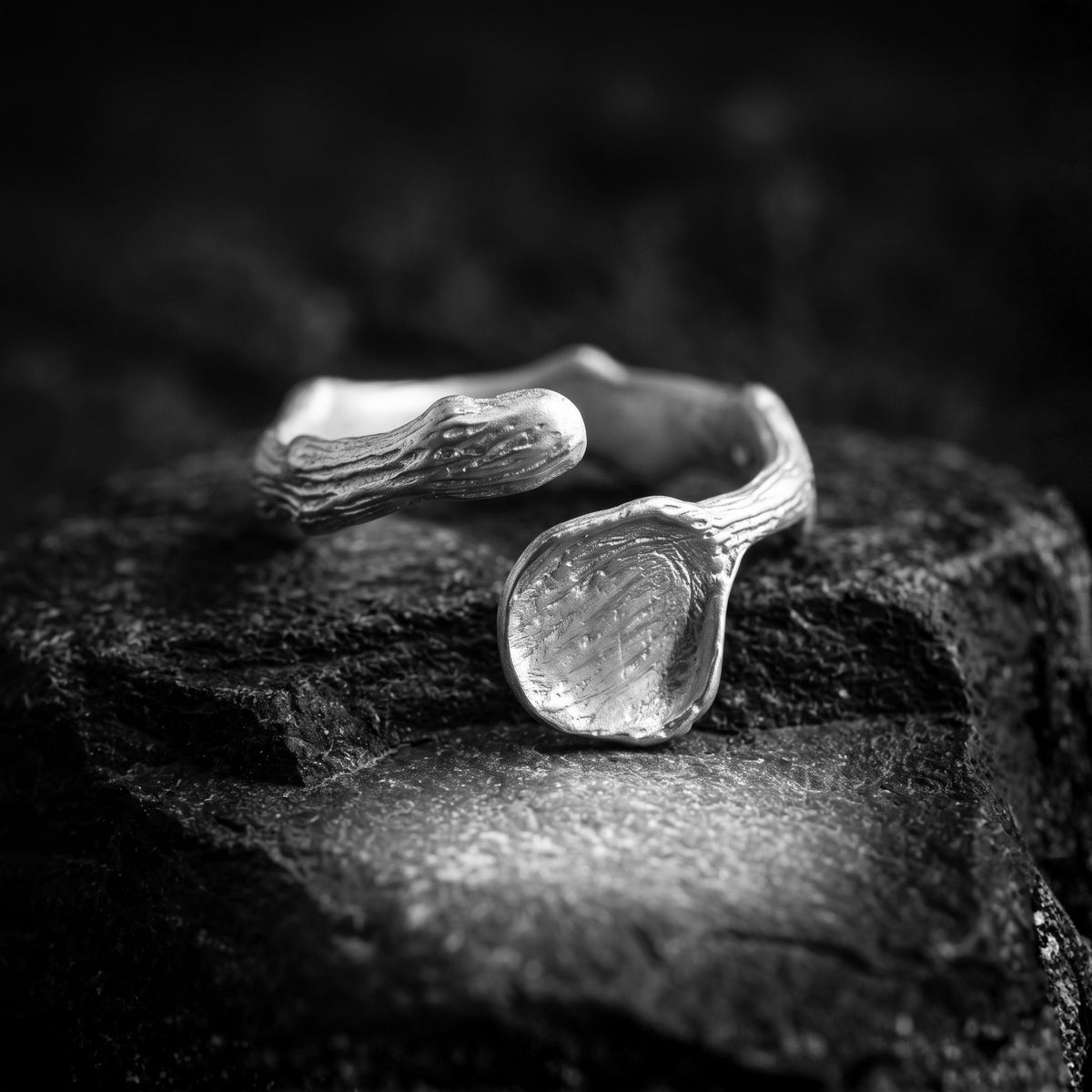 Silver open ring with bark-inspired texture and a flared end resting on dark textured rock.
