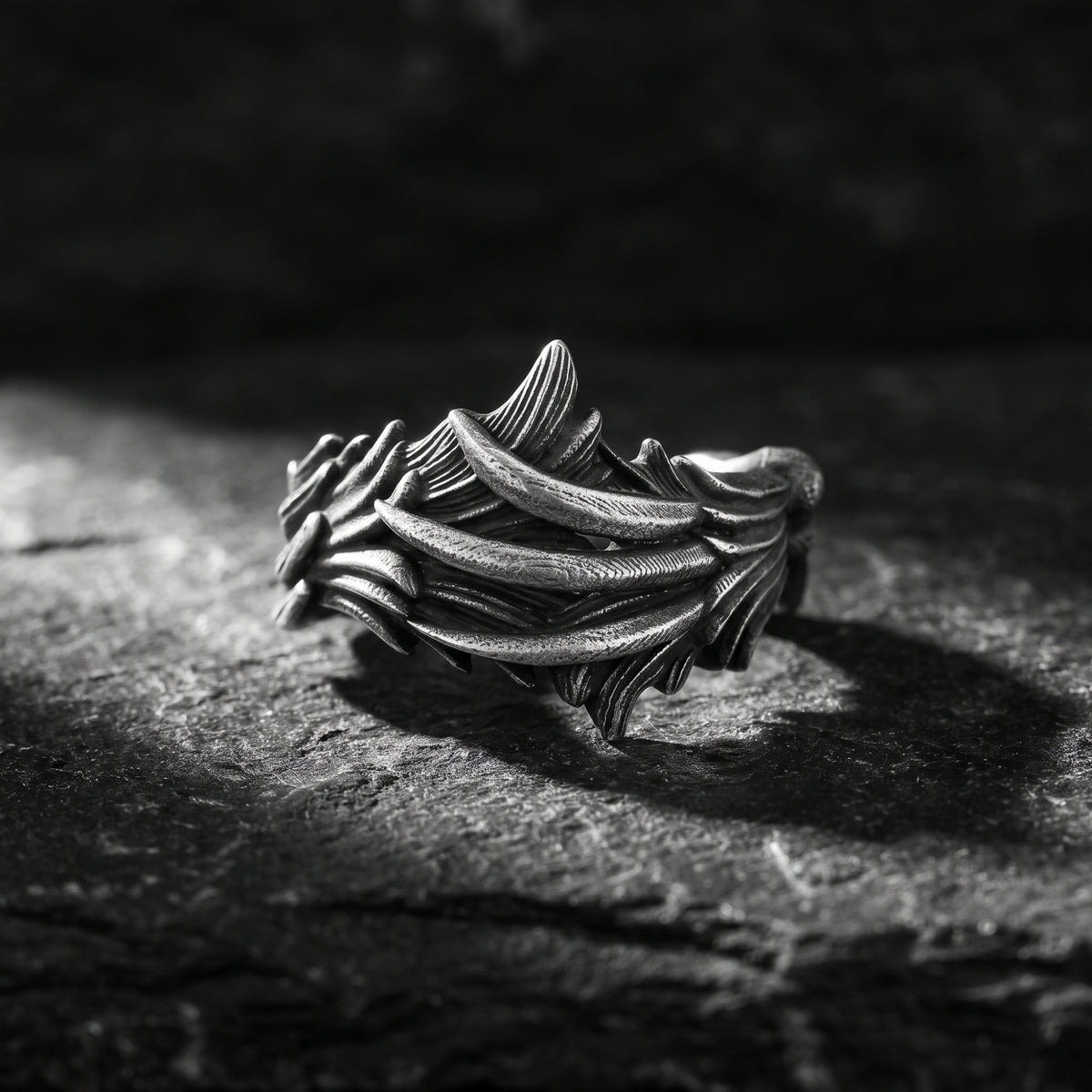 Antiqued silver feather open band ring standing on a dark textured rock.