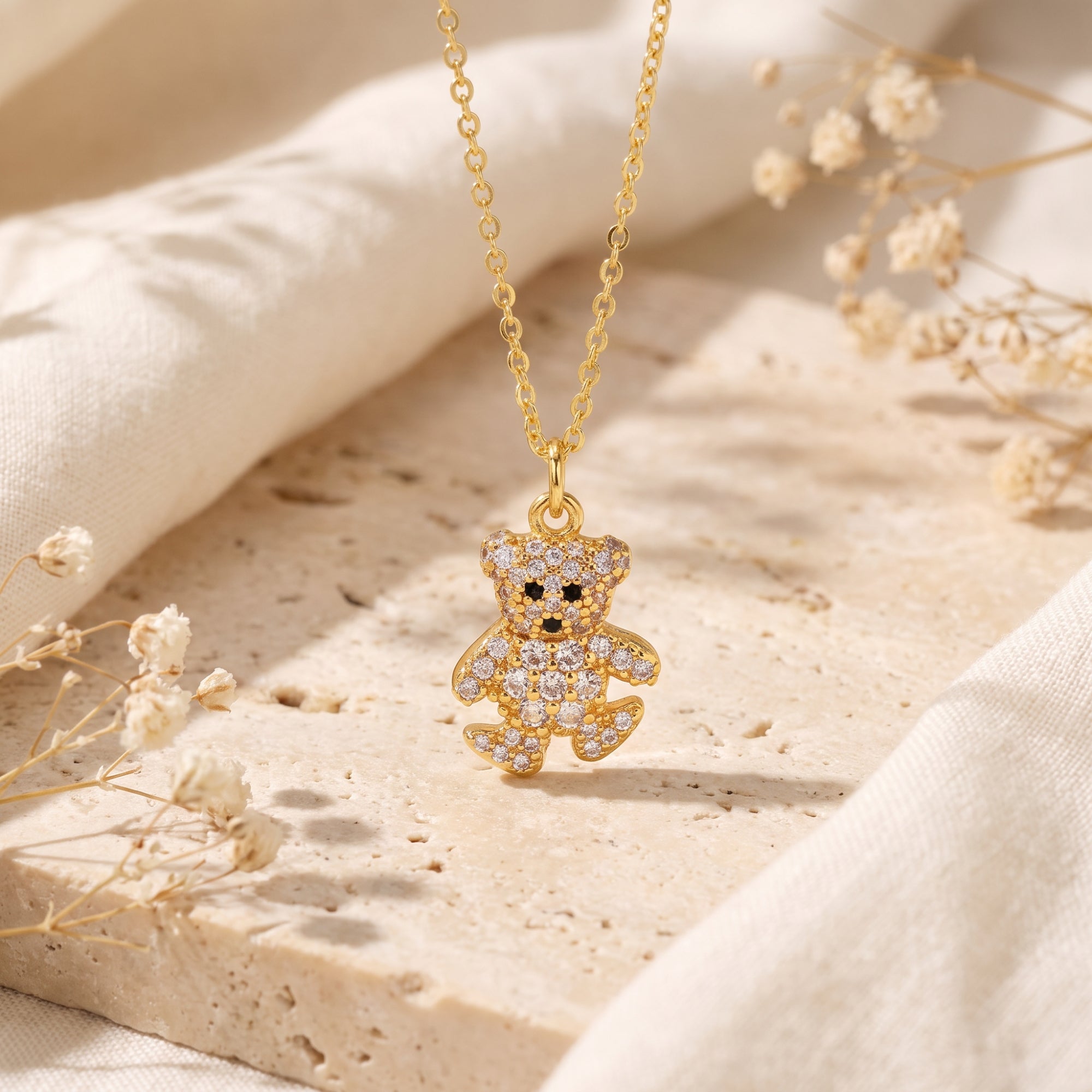 Gold-tone crystal teddy bear pendant necklace suspended above a textured beige stone block.