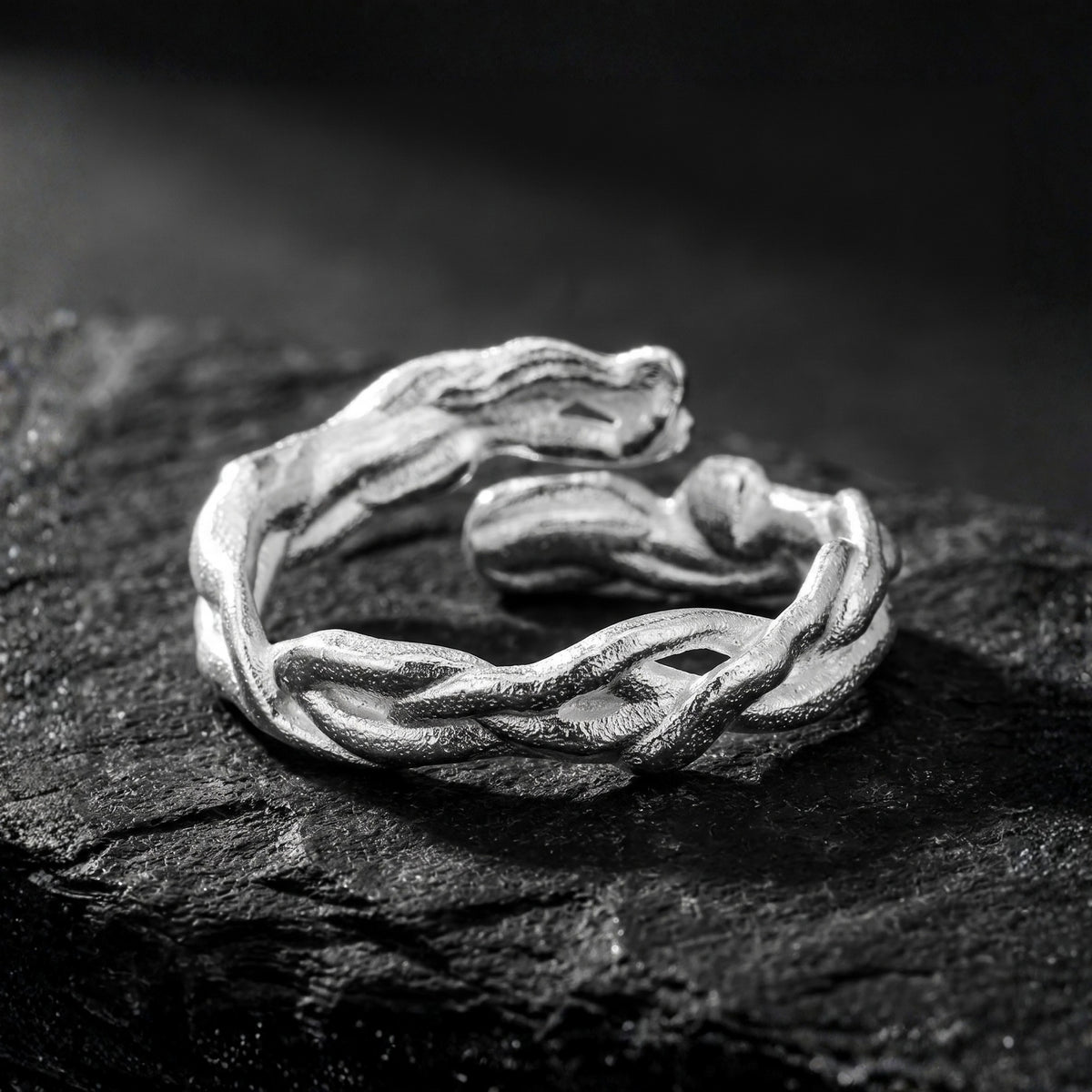 Silver open ring with sculpted woven strands resting on a dark slate surface.