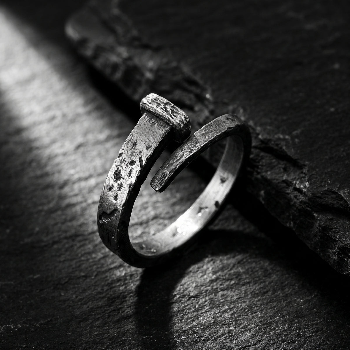 Close-up of a textured silver nail-style open-band ring resting on a dark textured surface.