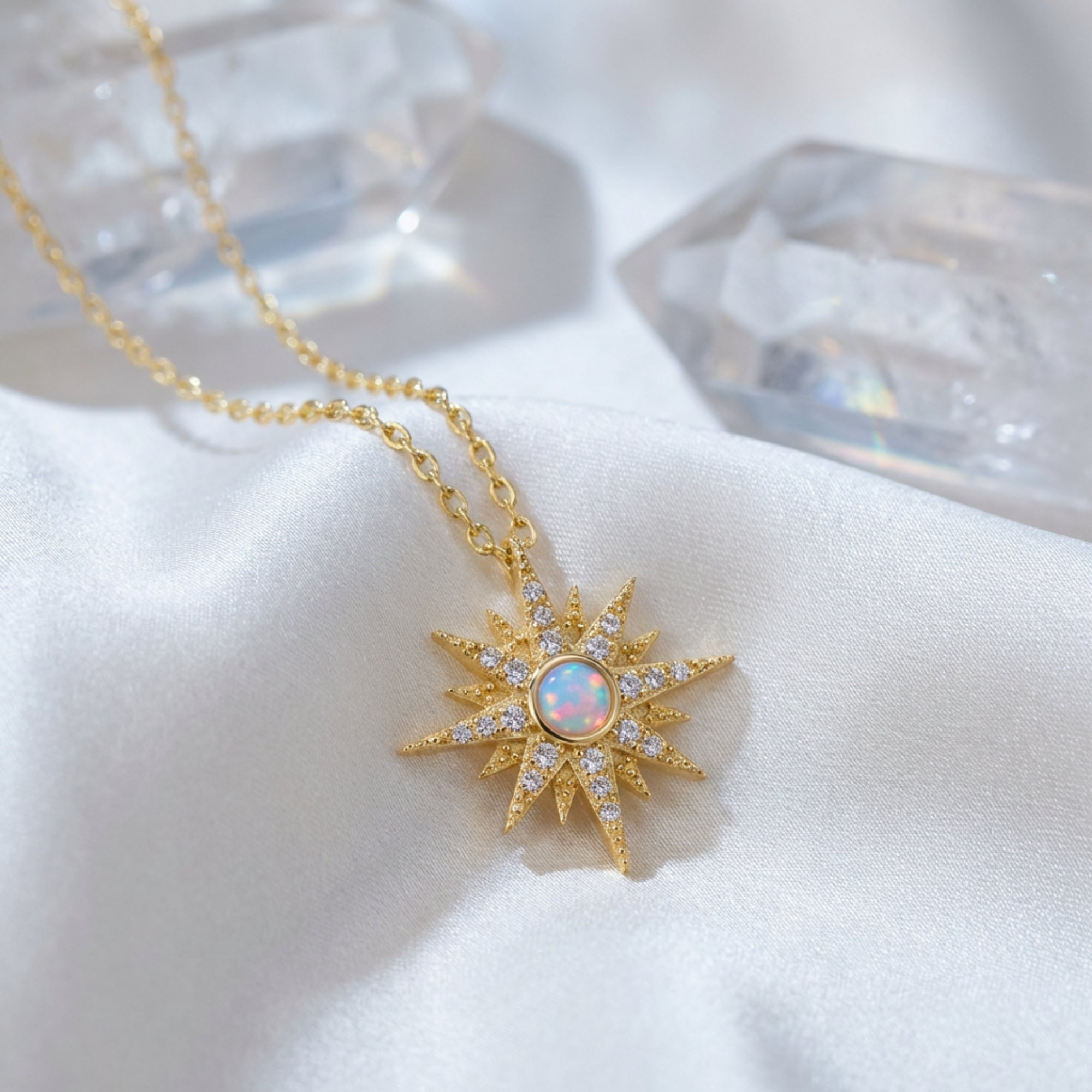 Gold starburst pendant necklace with a round white opal center on white silk fabric with crystal accents.