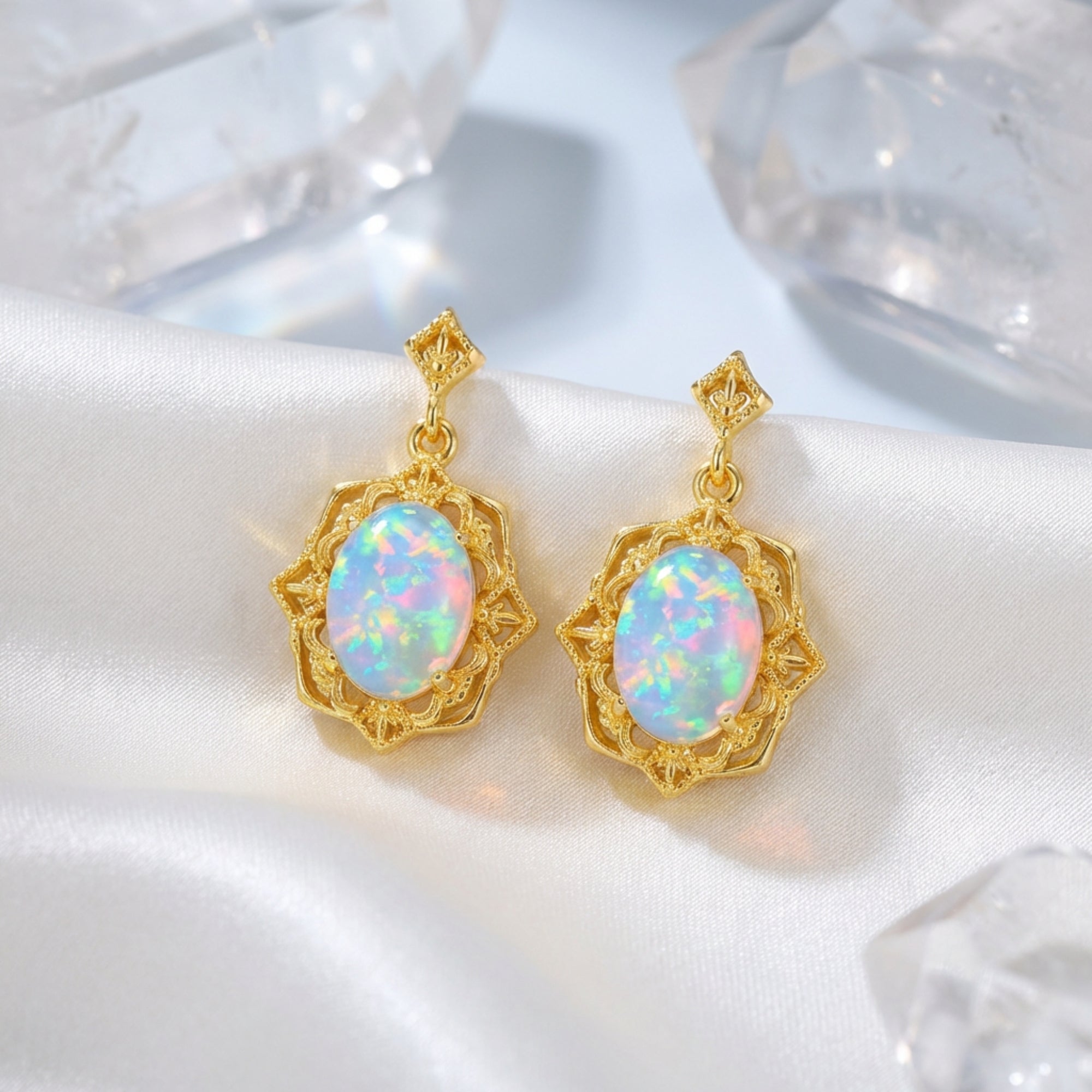 Gold-tone S925 silver drop earrings with oval white opals on white silk fabric with decorative crystals.