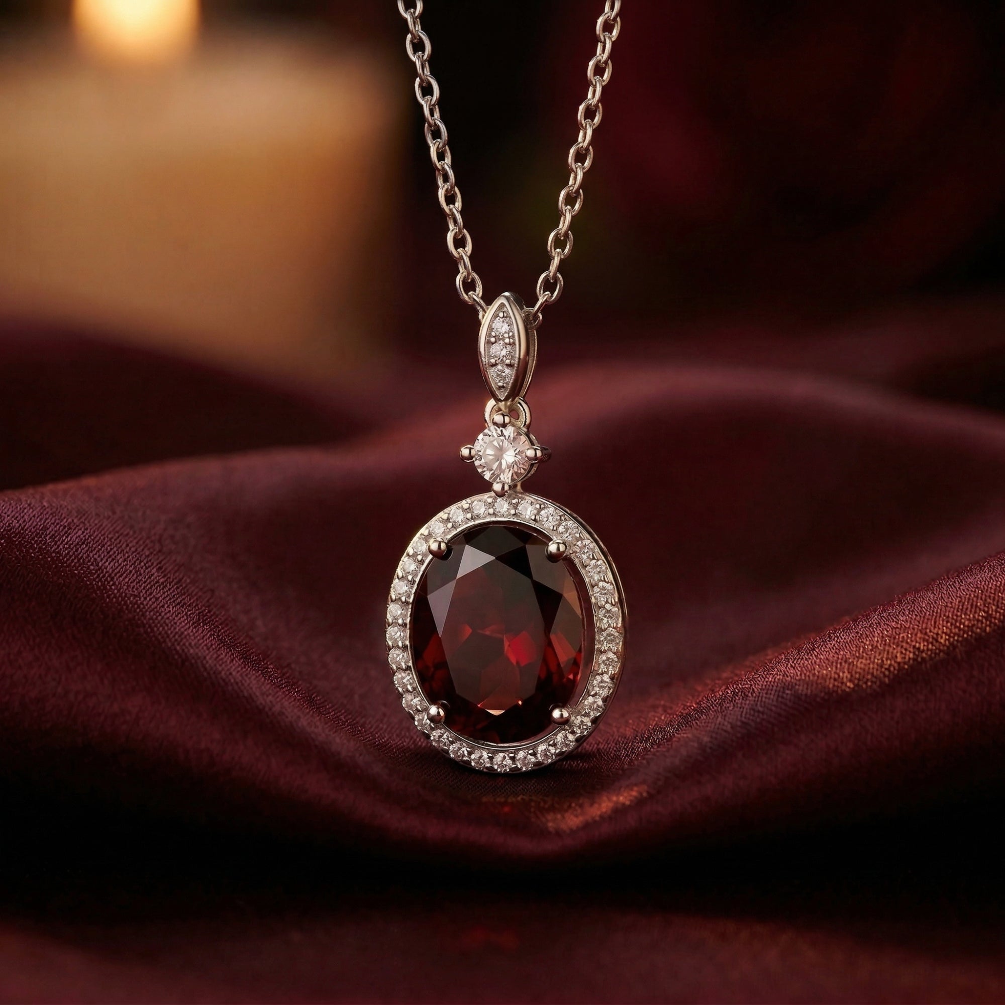 Oval-cut garnet necklace in S925 sterling silver resting on elegant burgundy fabric.
