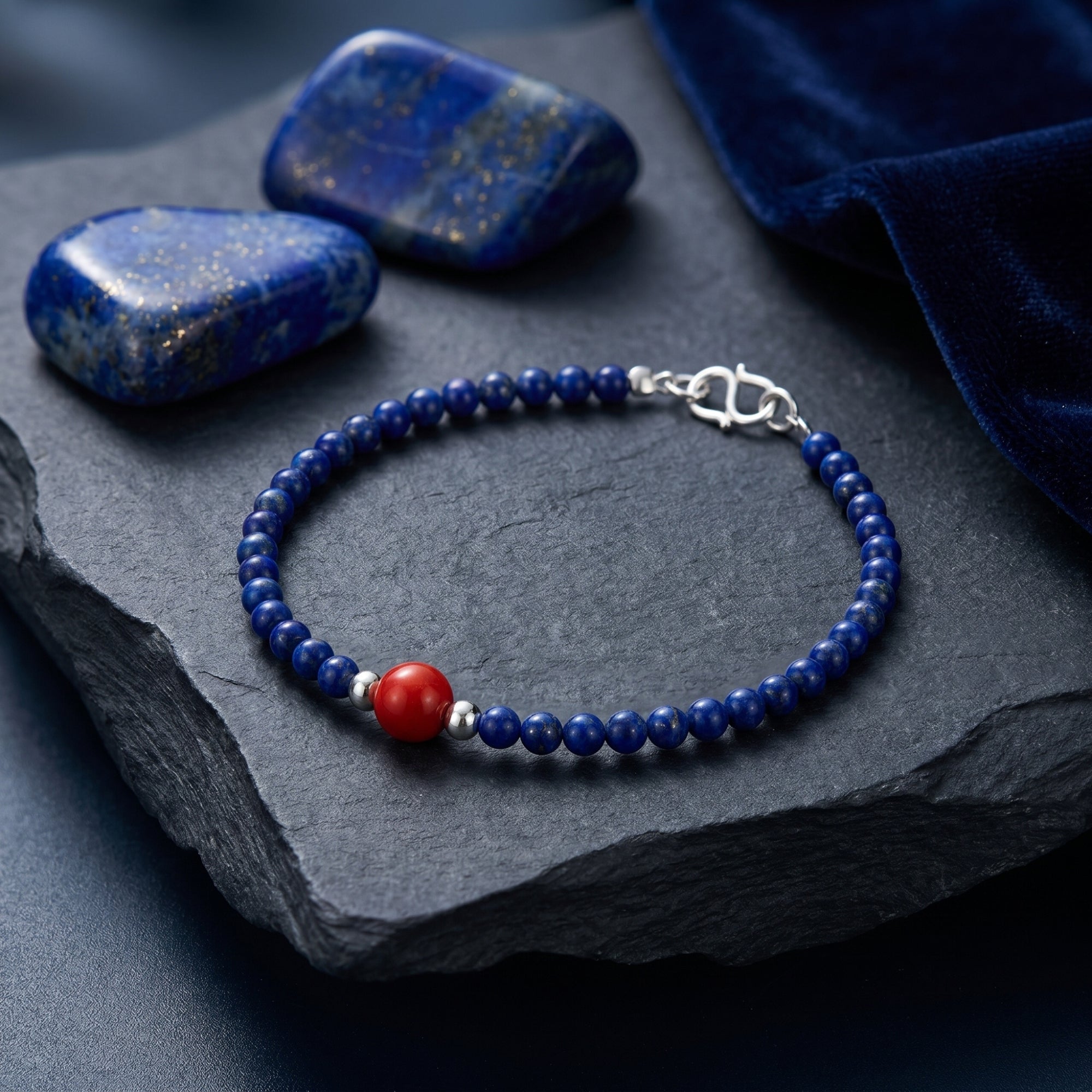 The Azure Trace natural round lapis bead bracelet with a red accent and silver clasp on a dark stone background.