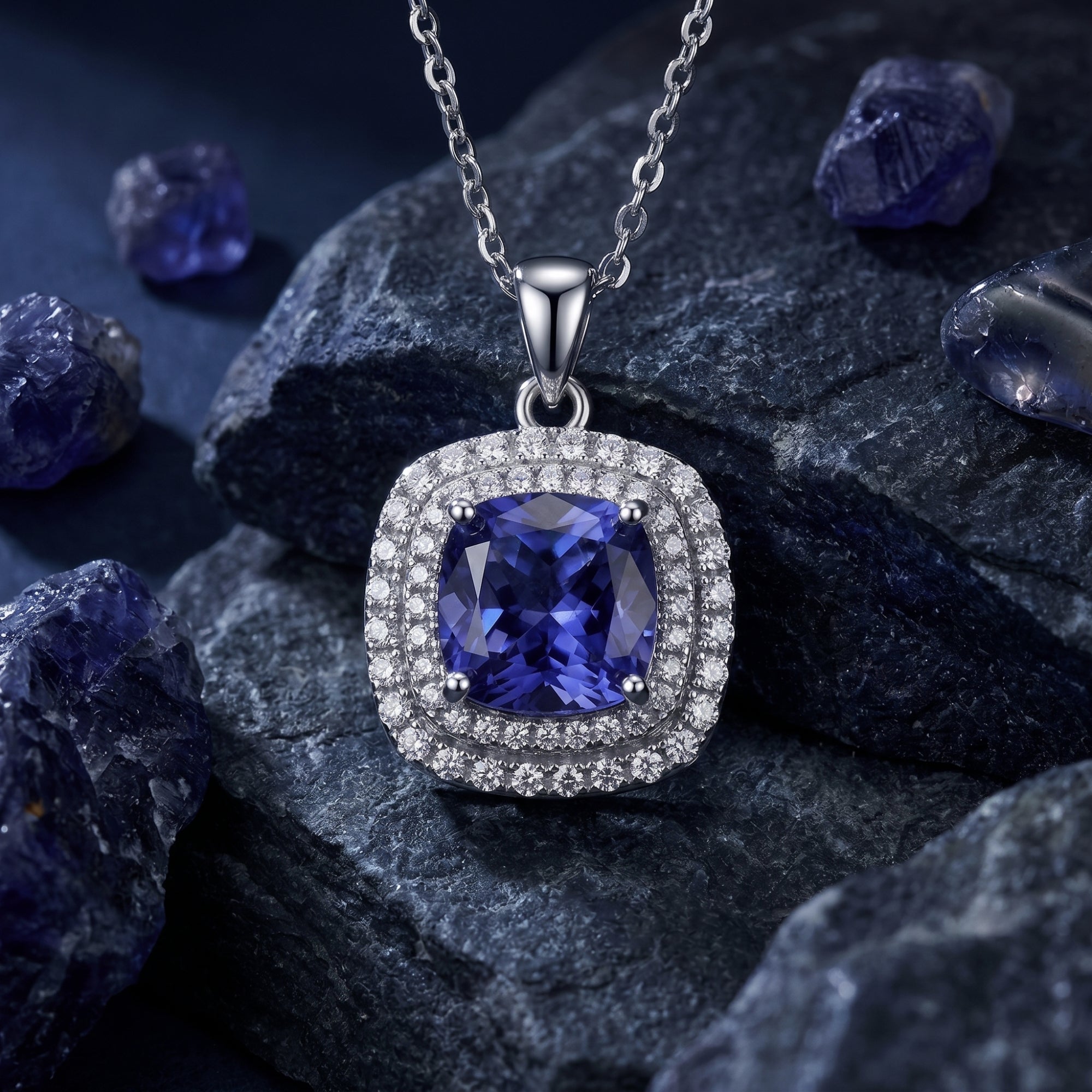 Cushion cut natural tanzanite necklace in white gold with double halo, styled on dark volcanic rocks.