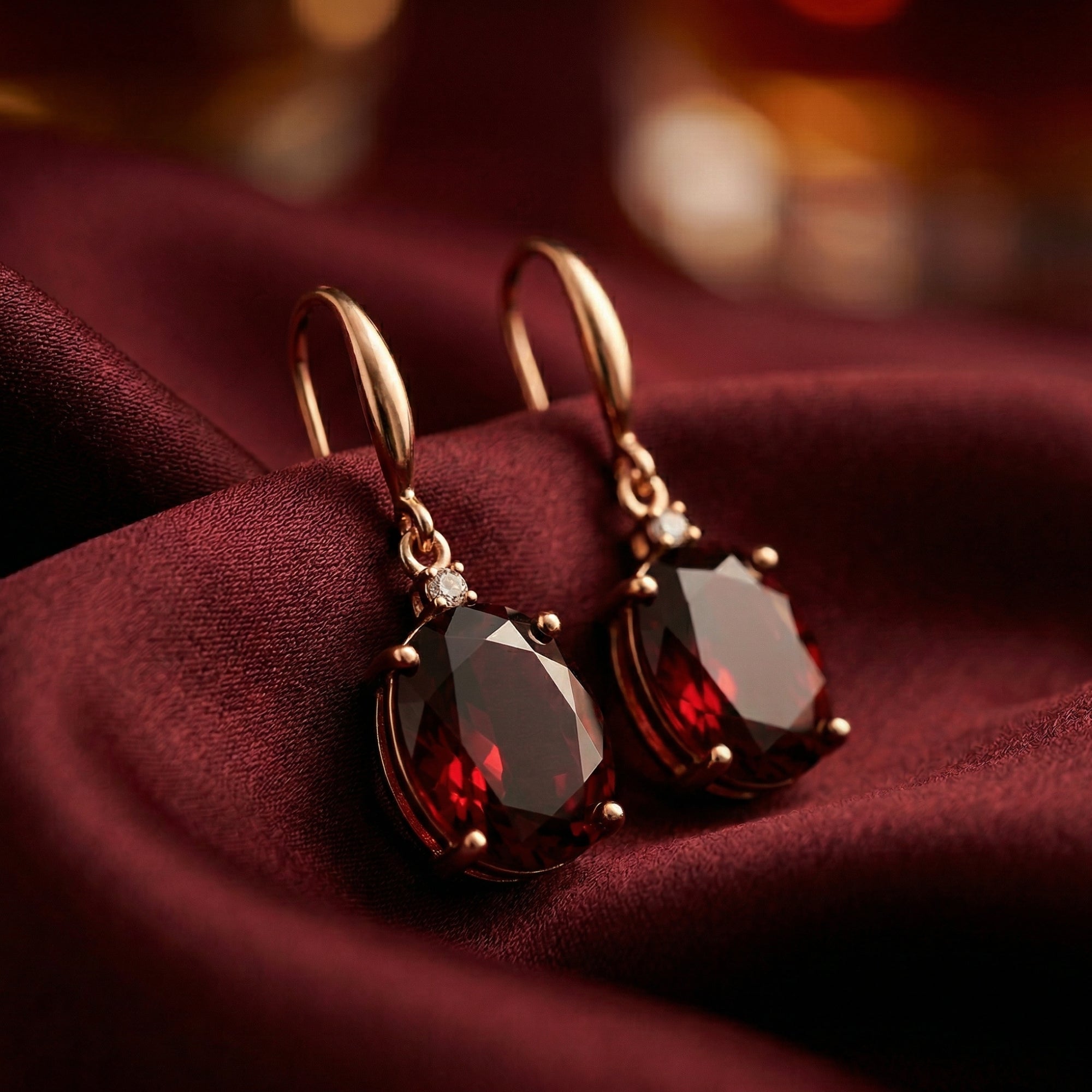 Macro view of the faceted oval cut natural garnets in 18K rose gold drop earrings on red fabric.