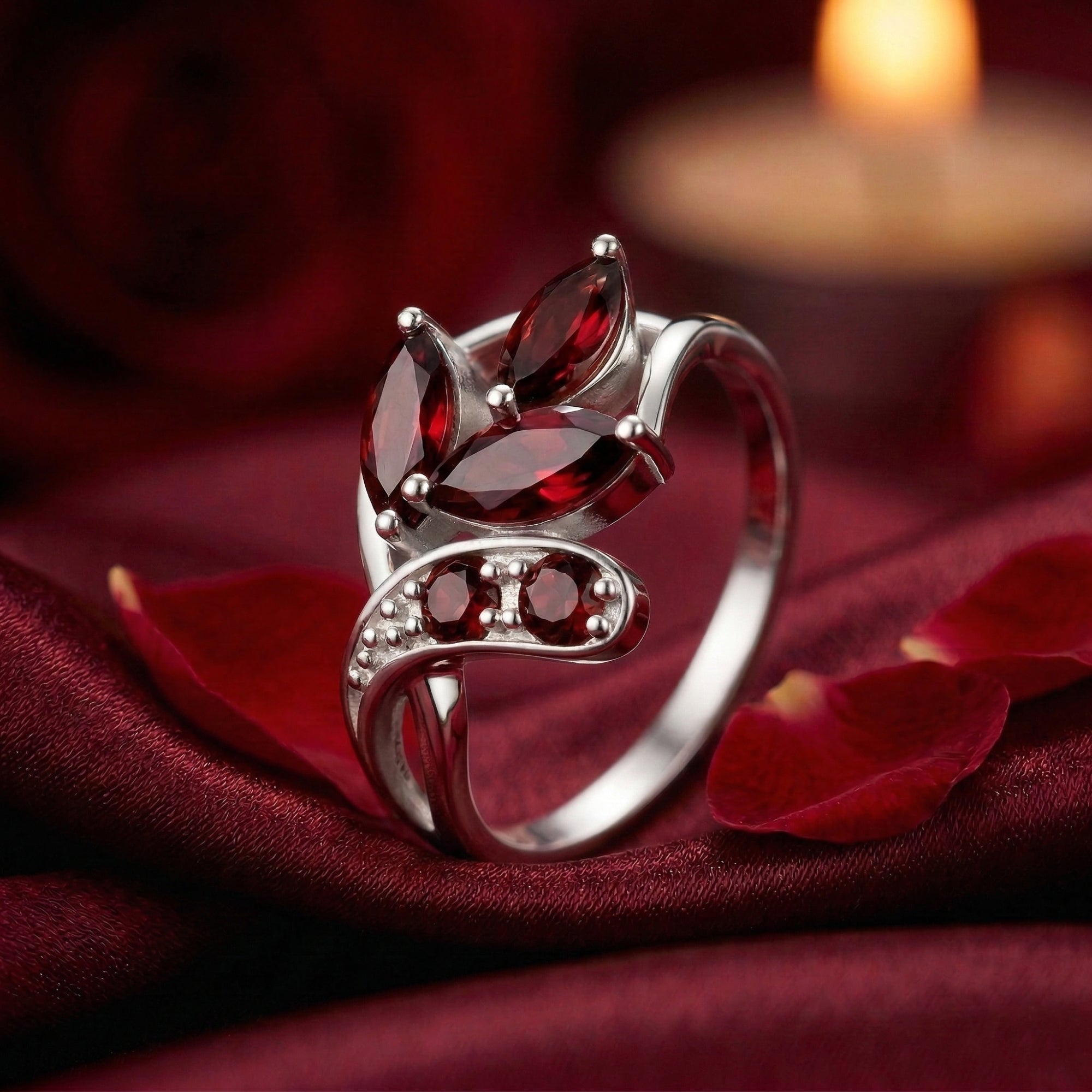 Elestria sterling silver bypass ring with marquise and round garnets on red silk with rose petals and a candle.
