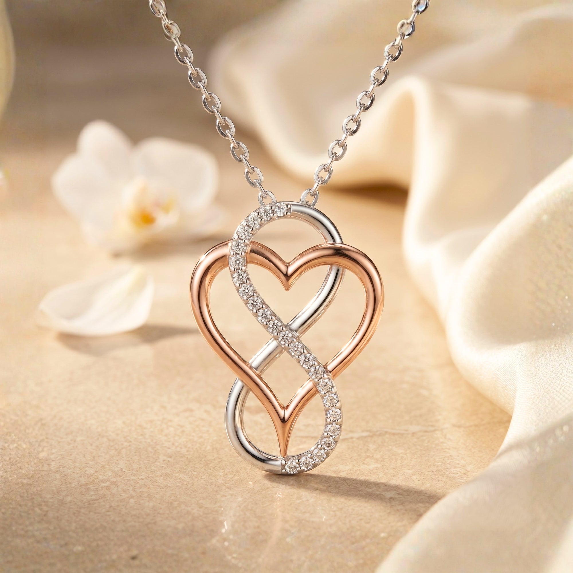 Two-tone infinity heart necklace with round moissanite on a draped fabric background.