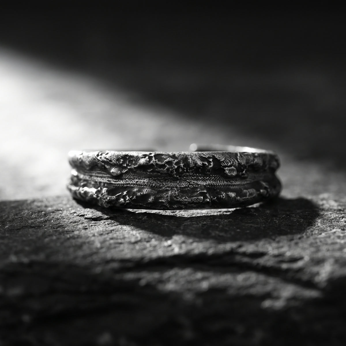 Textured silver ring resting horizontally on a rough stone surface in dramatic light.