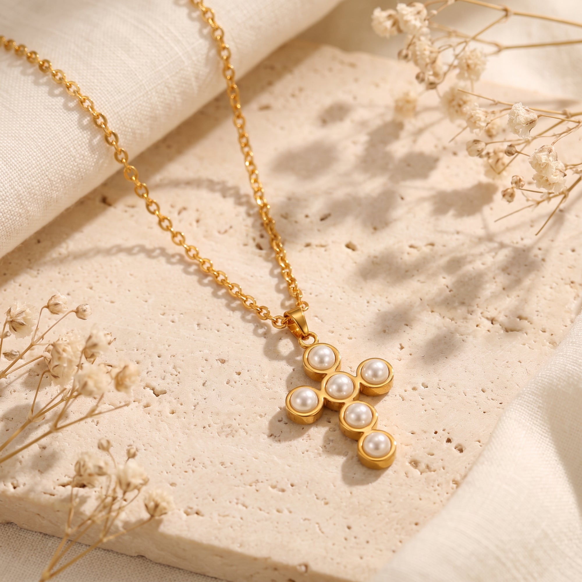 Detailed view of the gold-tone cross pendant set with six white simulated pearls on a textured stone block.