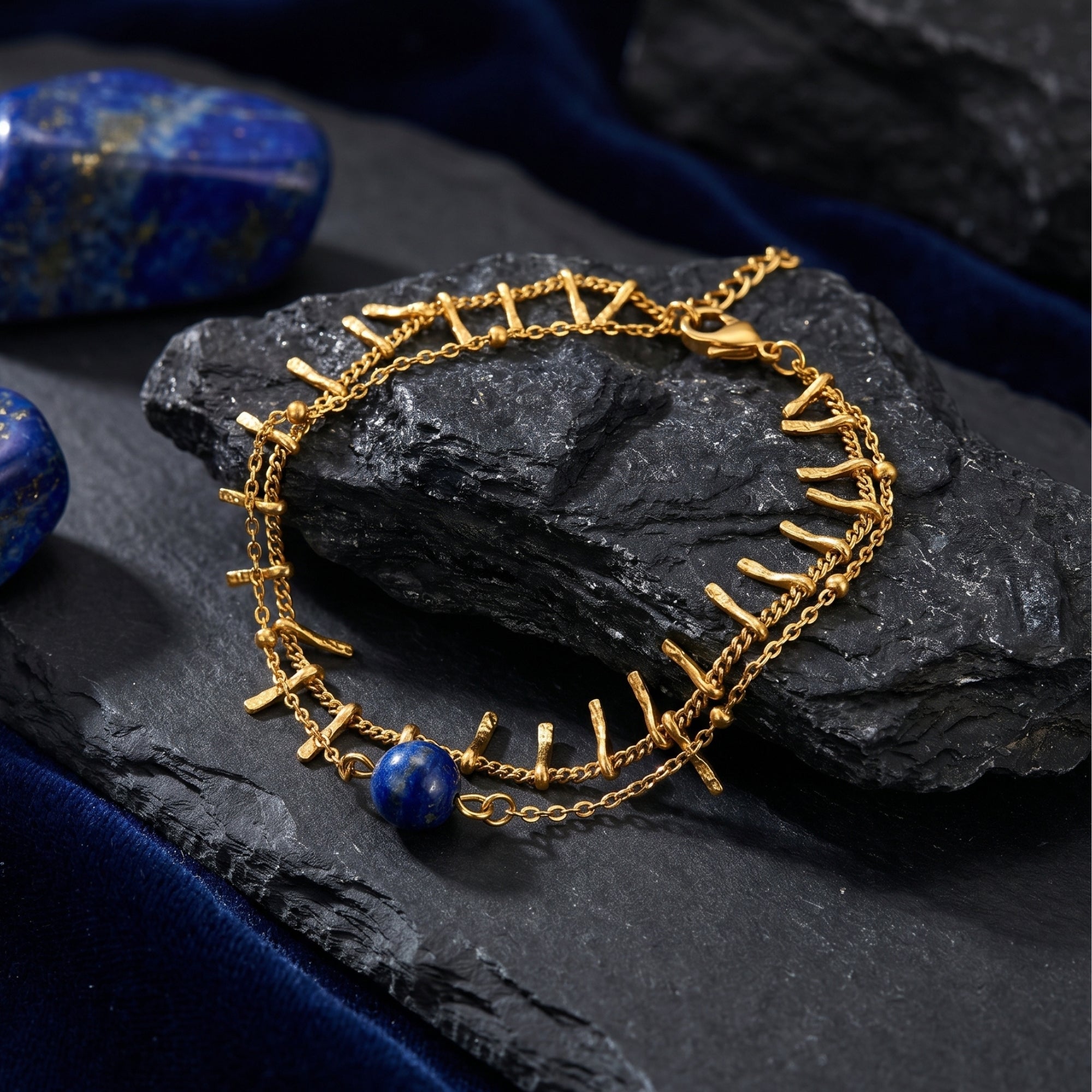 18K gold plated stainless steel bracelet with a round lapis lazuli bead on a dark textured rock.