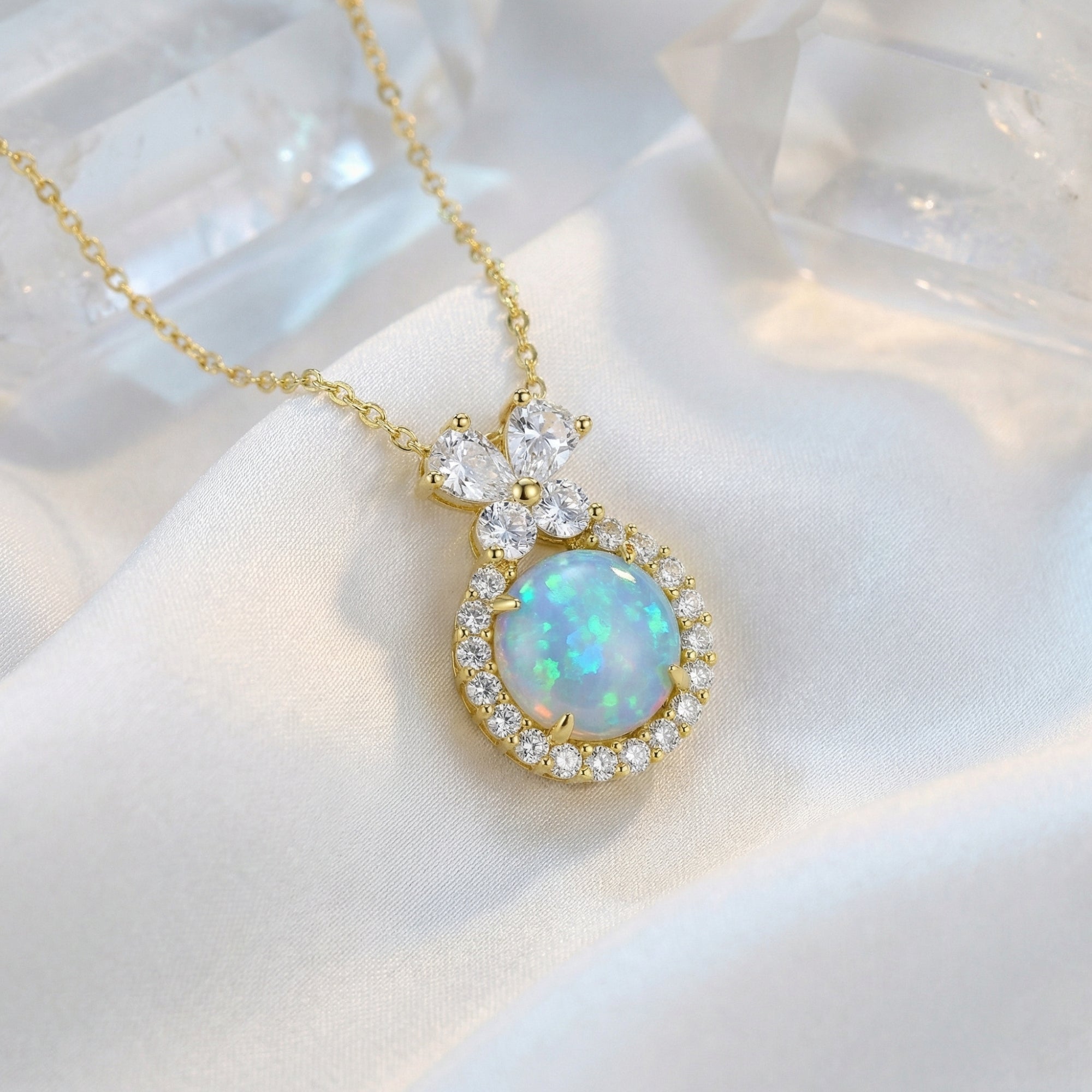 Gold vermeil pendant necklace with a round blue opal and crystal halo styled on white silk with crystals.