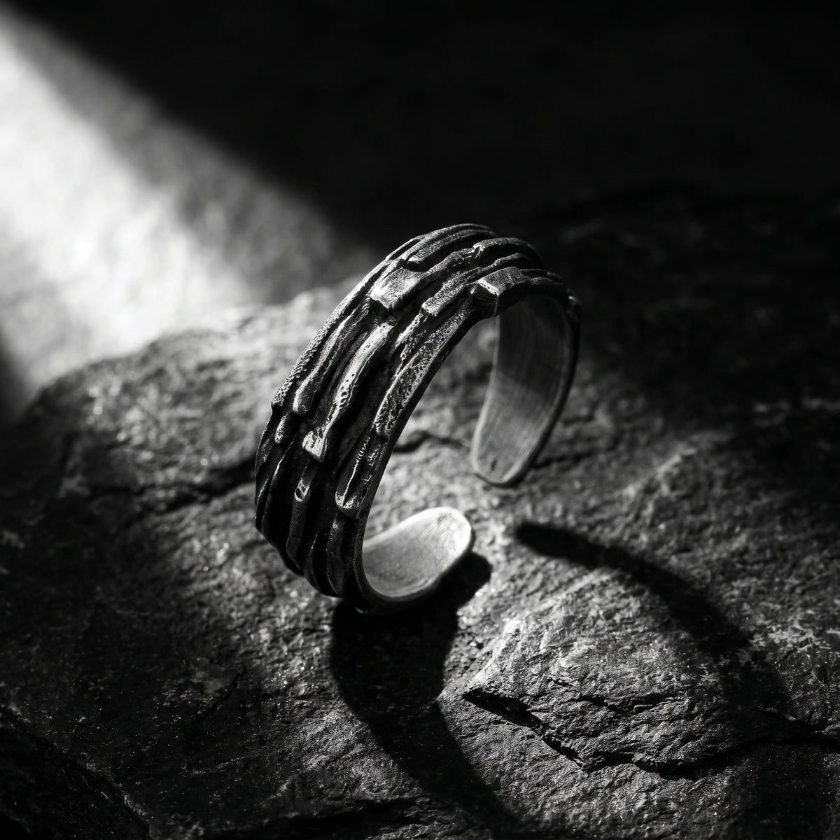 Textured oxidized silver open band ring standing upright at an angle on a dark stone surface.