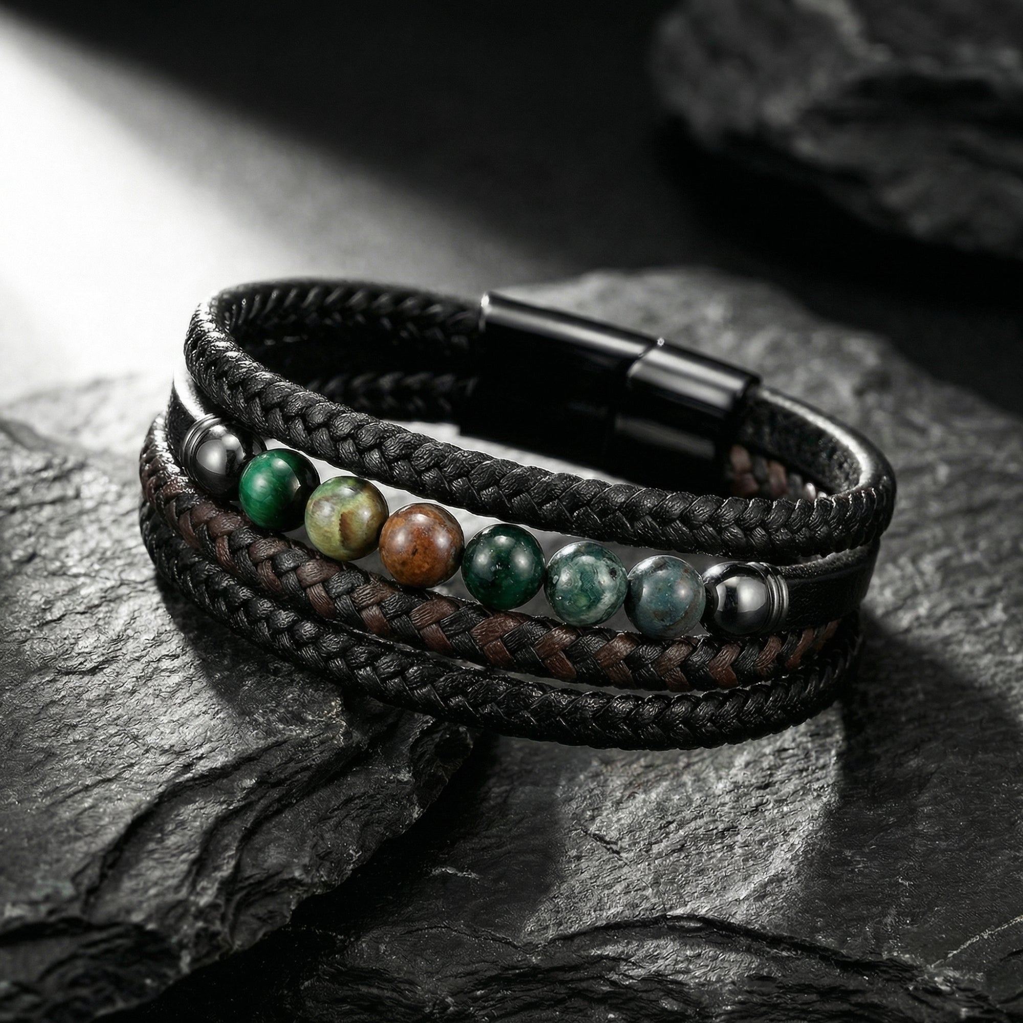 Multi-strand black and brown braided leather bracelet with black stainless steel clasp and stone beads on slate rocks.