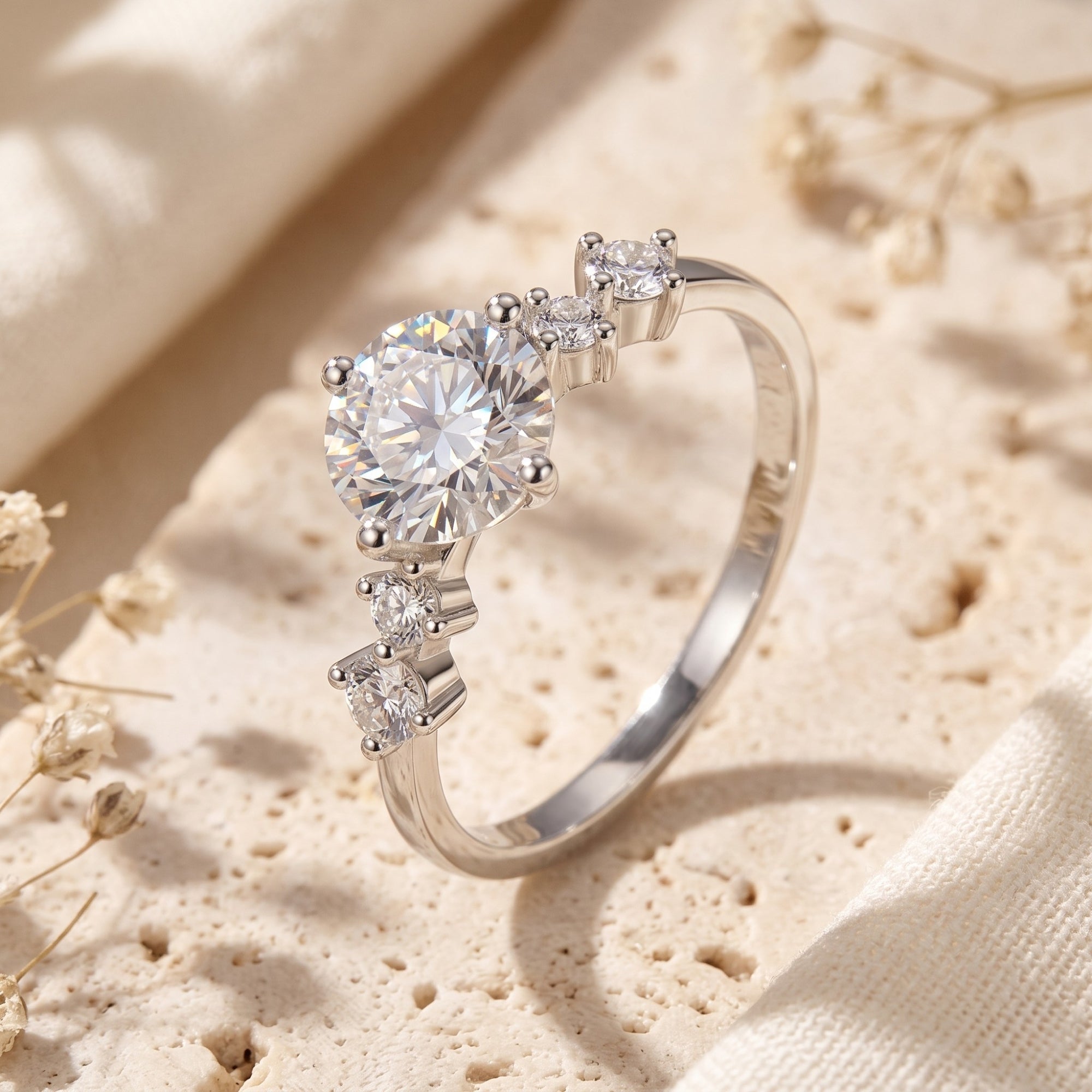 Close-up of a silver solitaire ring with a round center stone and graduating accent stones on a beige stone surface.