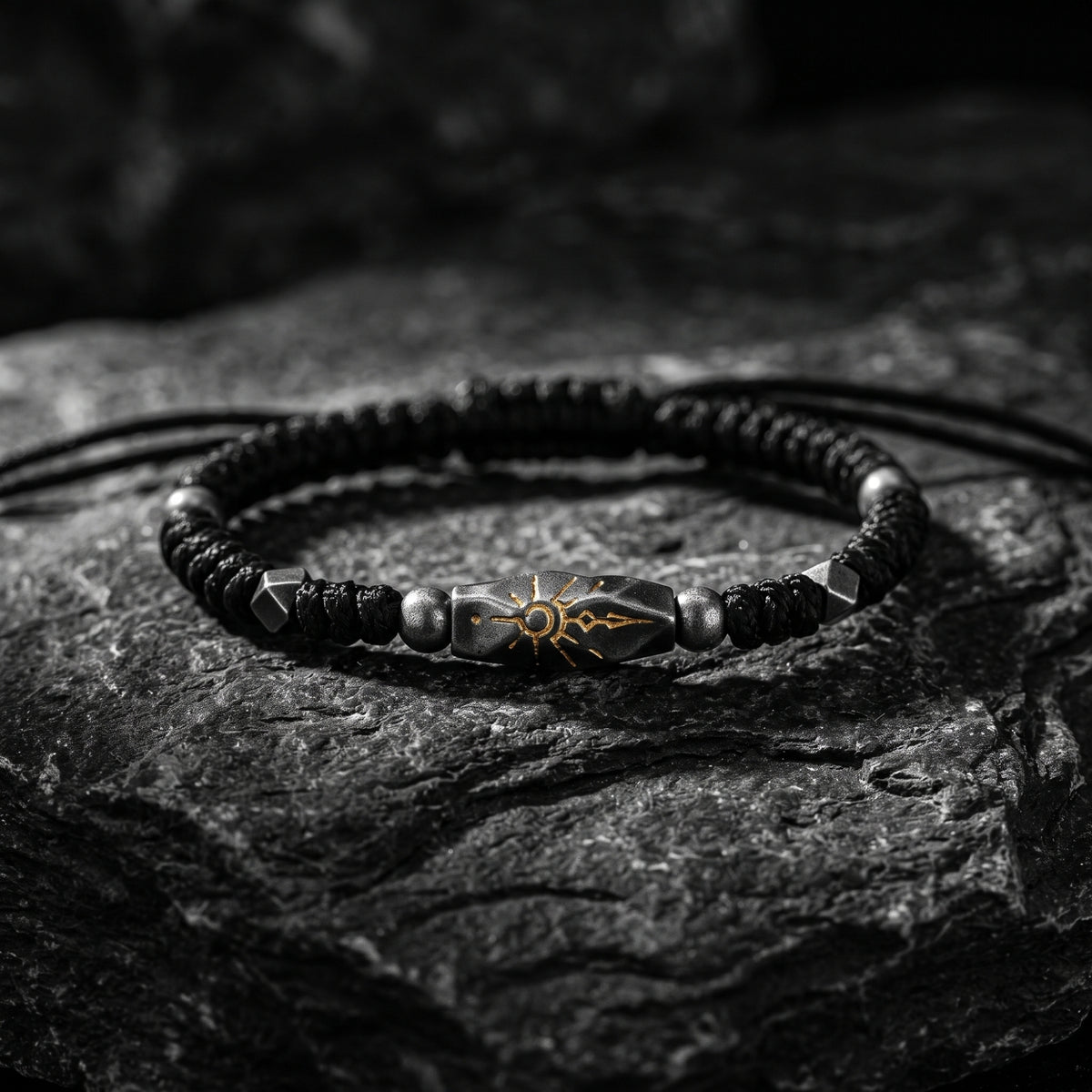 Sunburst rope bracelet resting on textured dark stone, showing its carved silver focal station and etched motif.