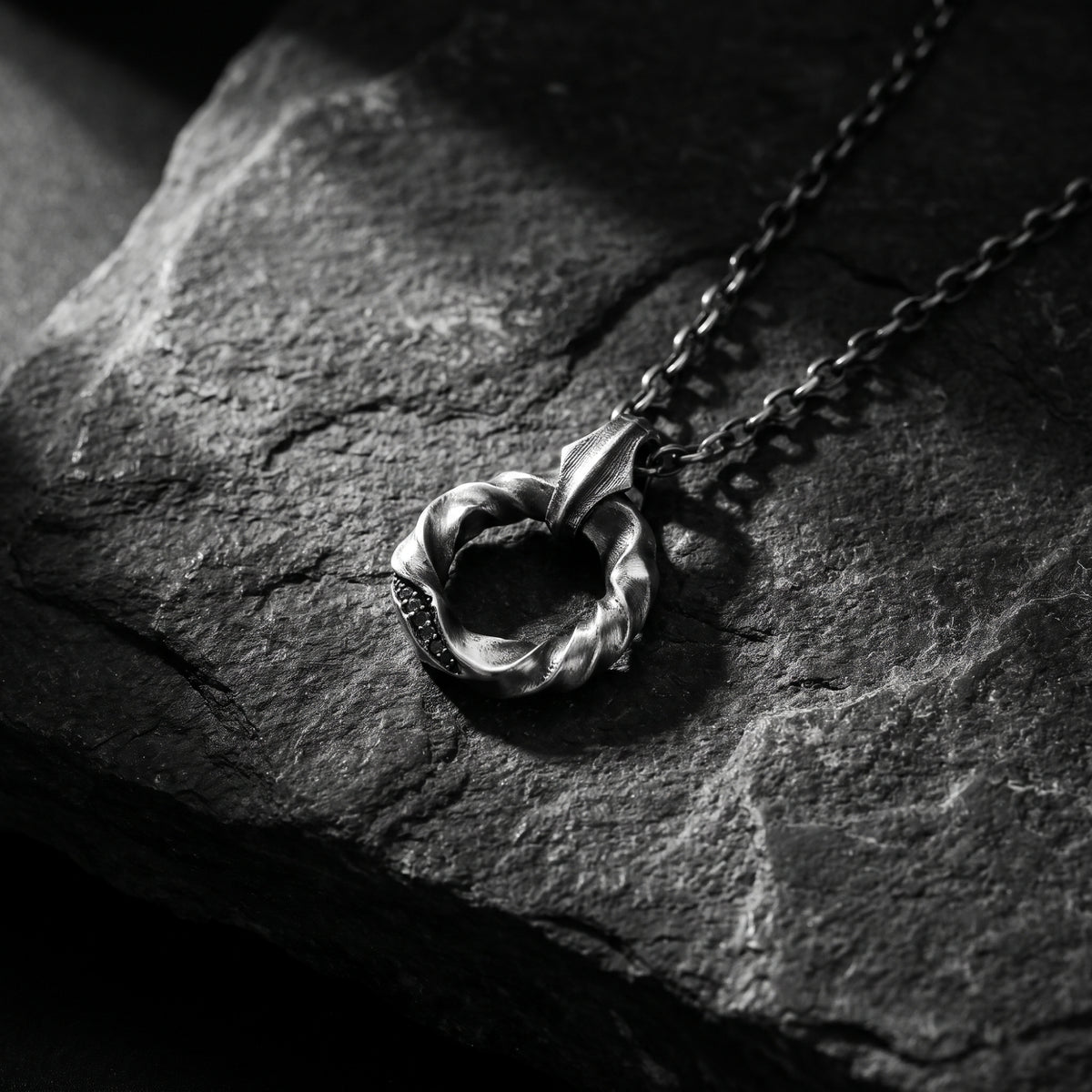 Twisted silver circle pendant necklace lying flat on a dark textured surface.