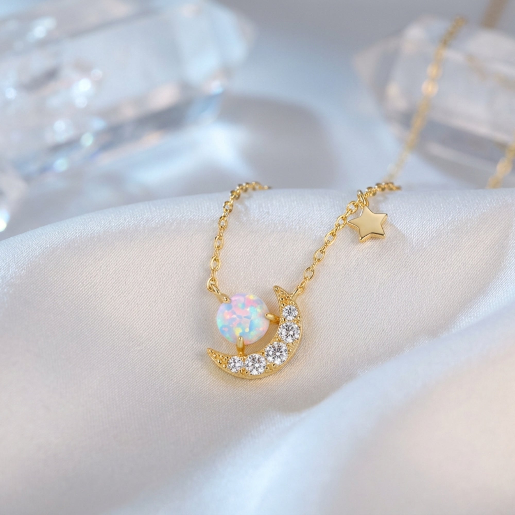 Gold vermeil Stellara necklace with round white opal and crescent moon pendant on white silk fabric.