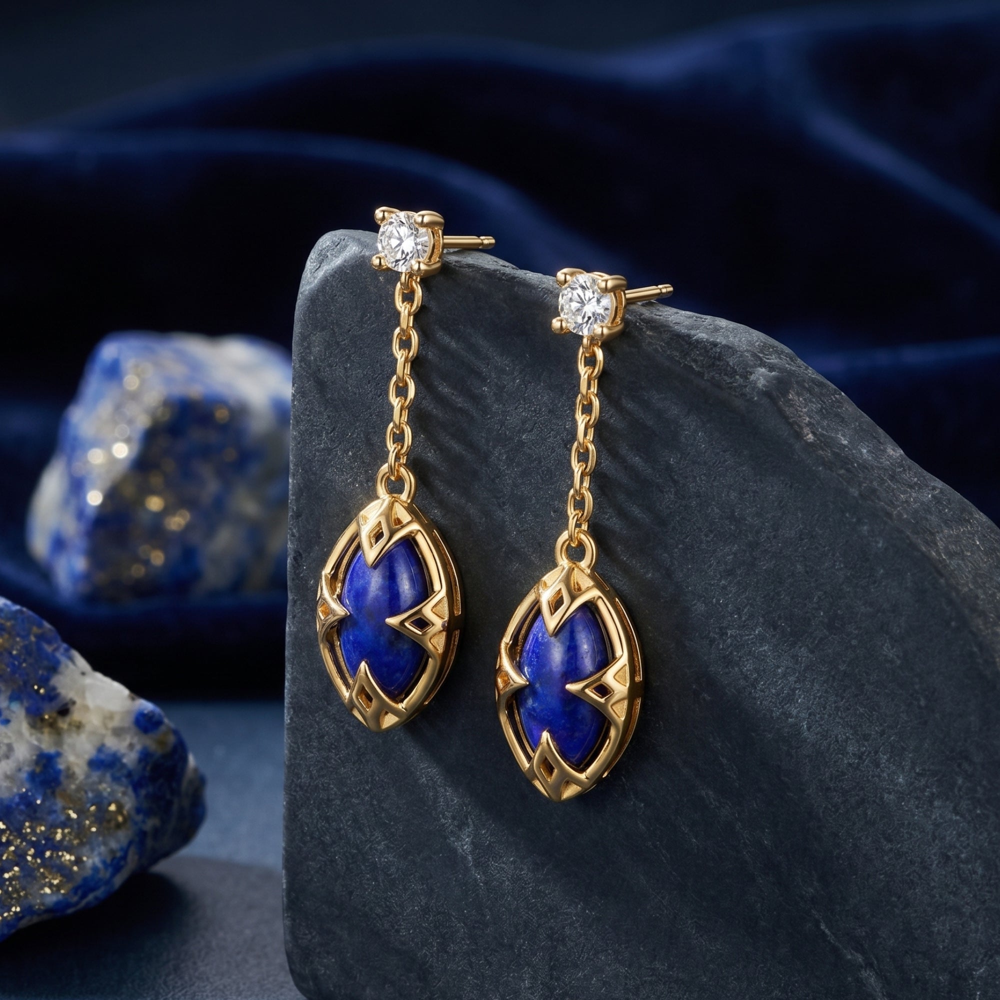 18k gold plated marquise lapis lazuli drop earrings hanging from a dark stone with blue velvet background.