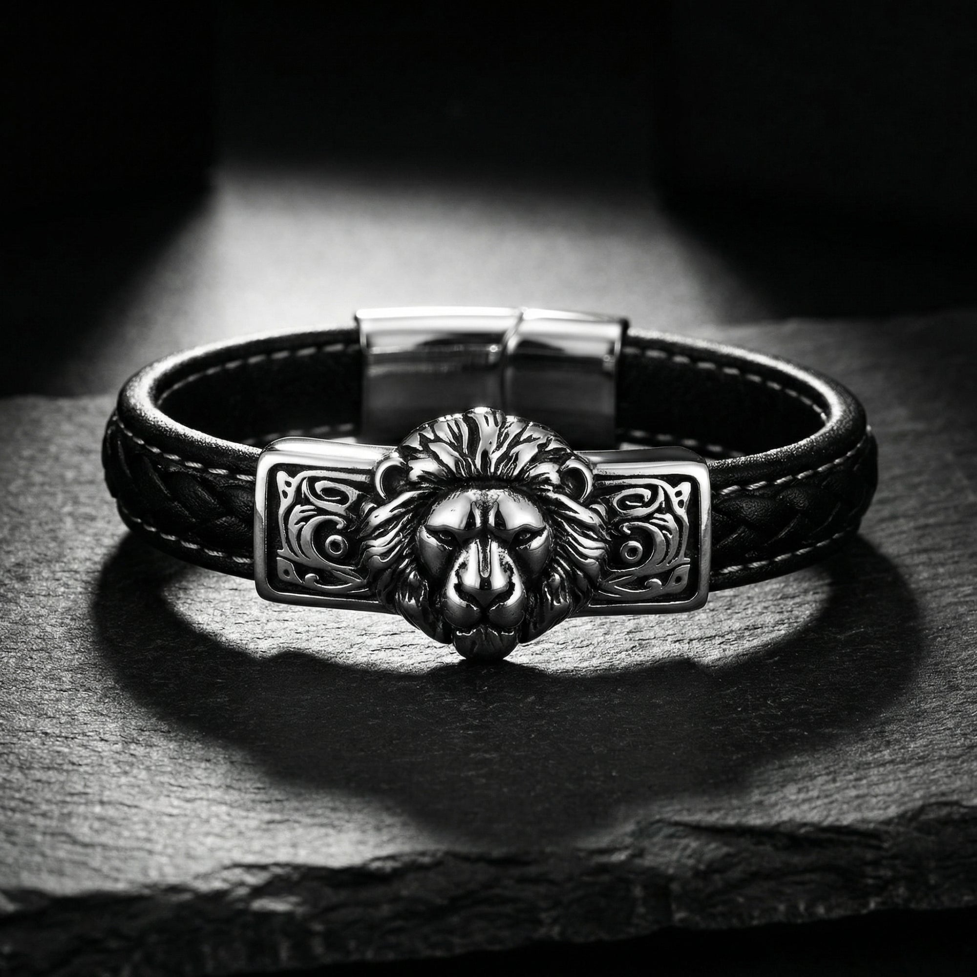 Men's braided black leather lion bracelet with a silver stainless steel centerpiece on a dark stone surface.