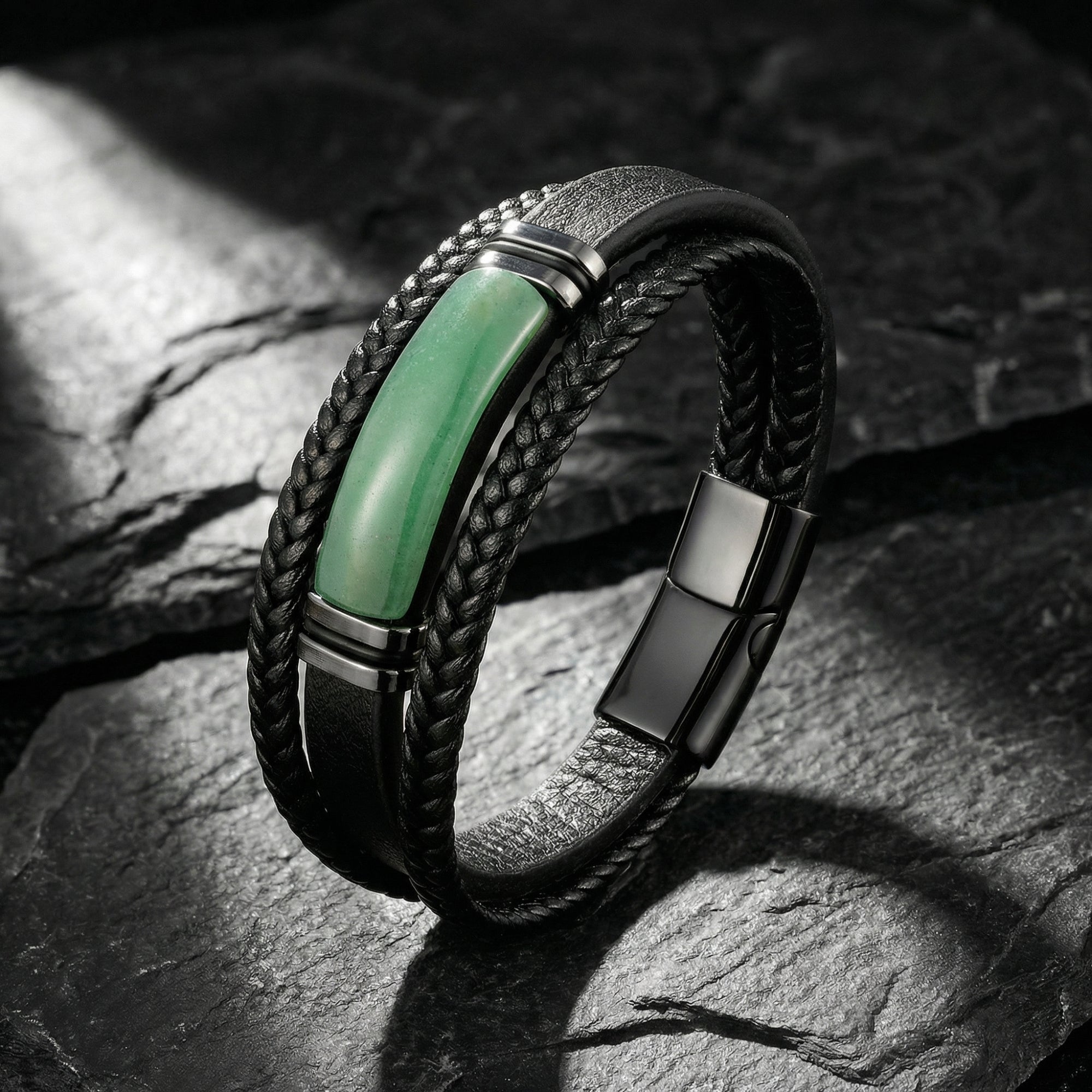 Angled view of a men's black braided leather bracelet with green stone centerpiece and 316L steel hardware on stone.
