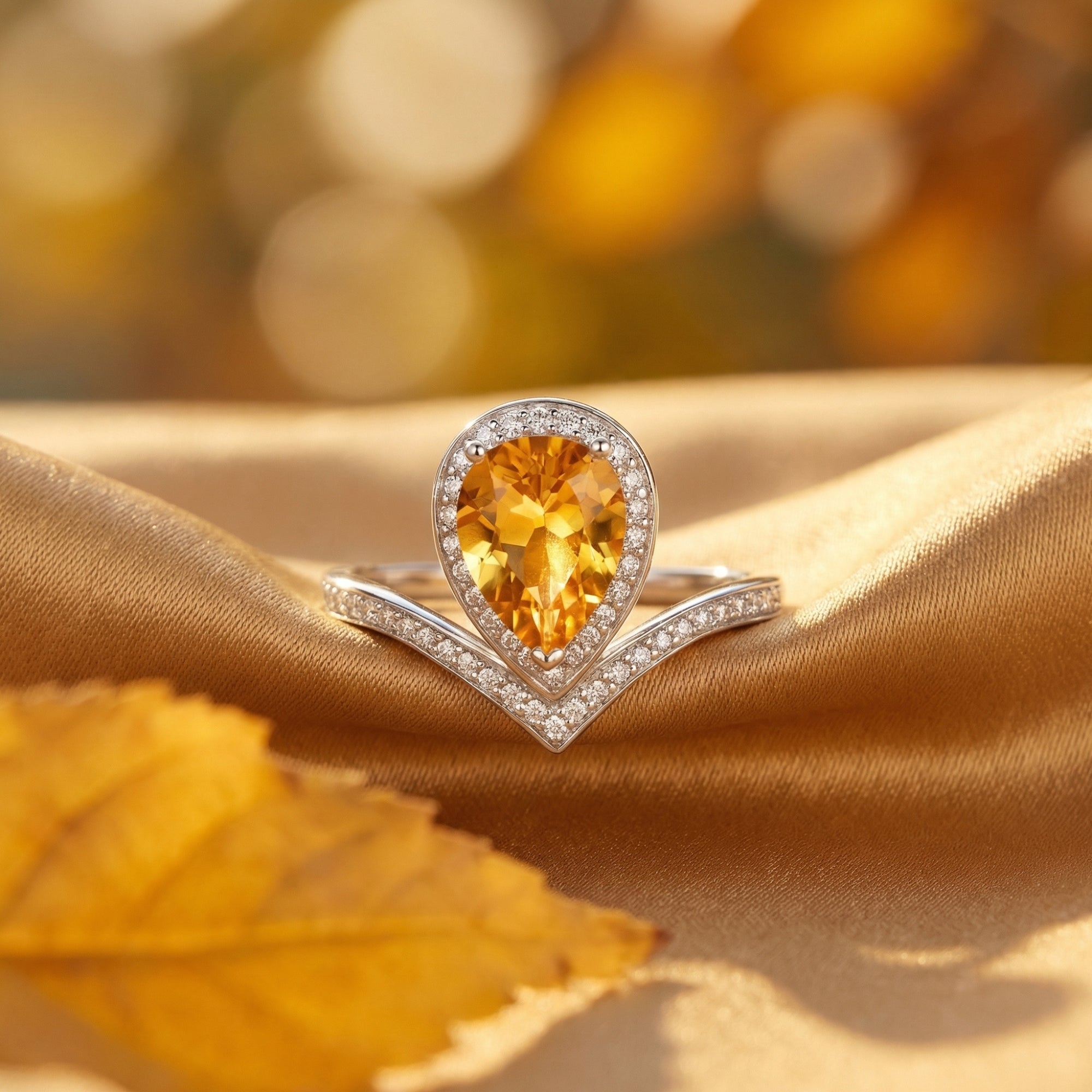 Pear cut natural citrine ring in sterling silver resting on golden fabric with an autumn leaf.