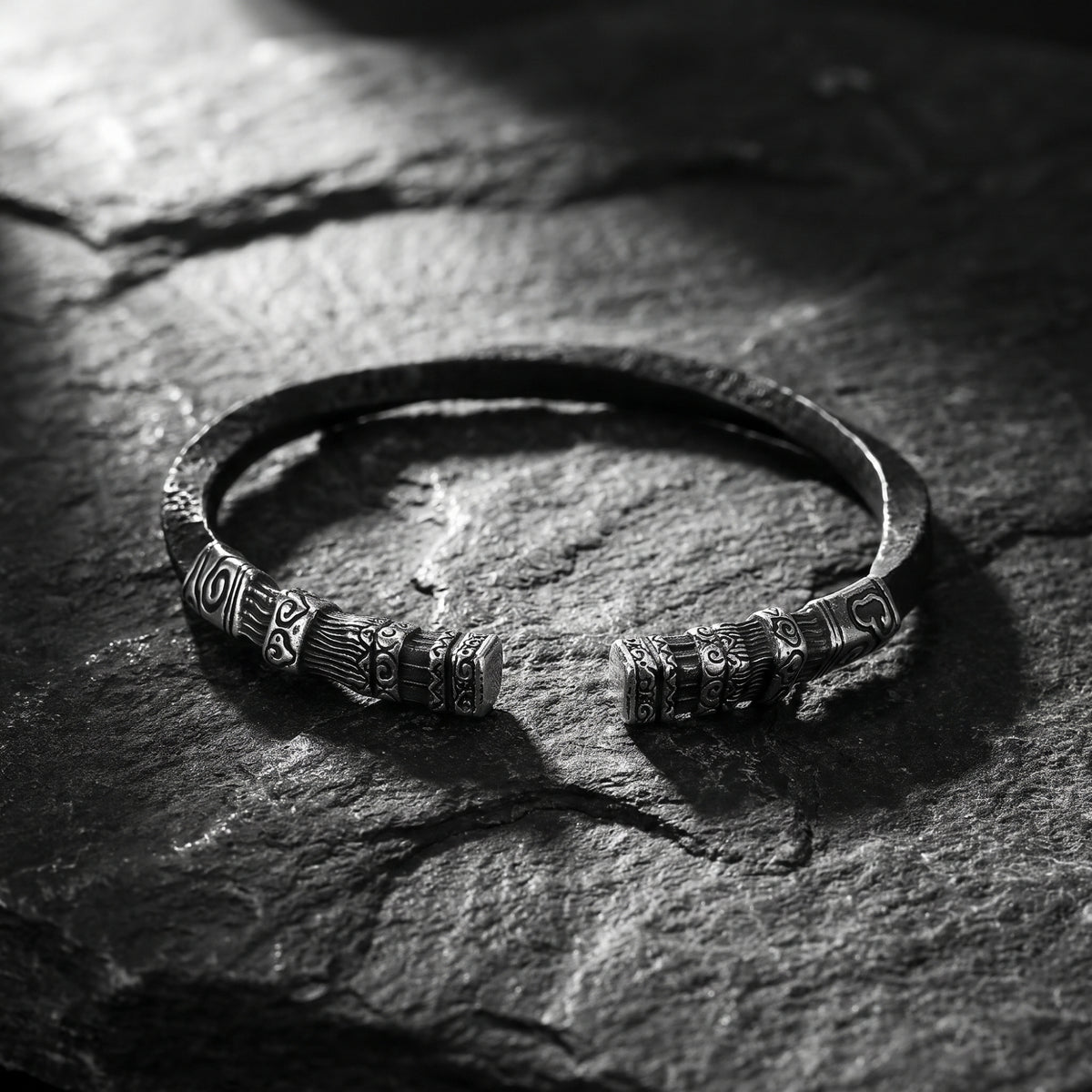 Carved Heritage open cuff bracelet on textured slate, viewed from above with carved ends in the foreground.