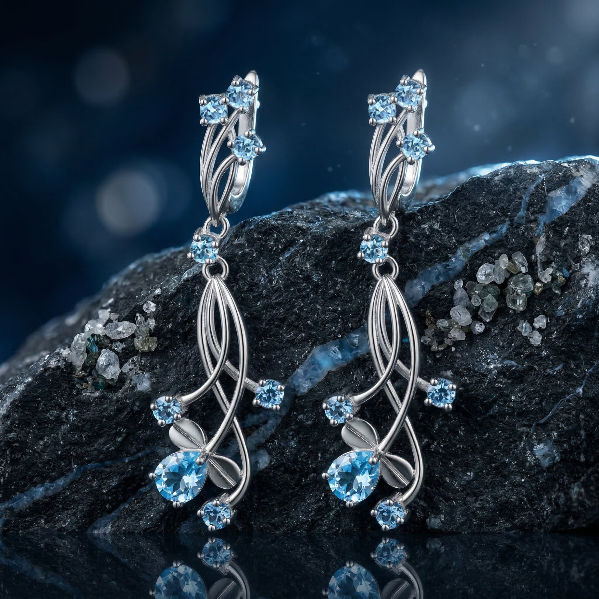 Oceanis Cascade silver drop earrings with pear and round cut blue topaz stones displayed on a dark oceanic rock.