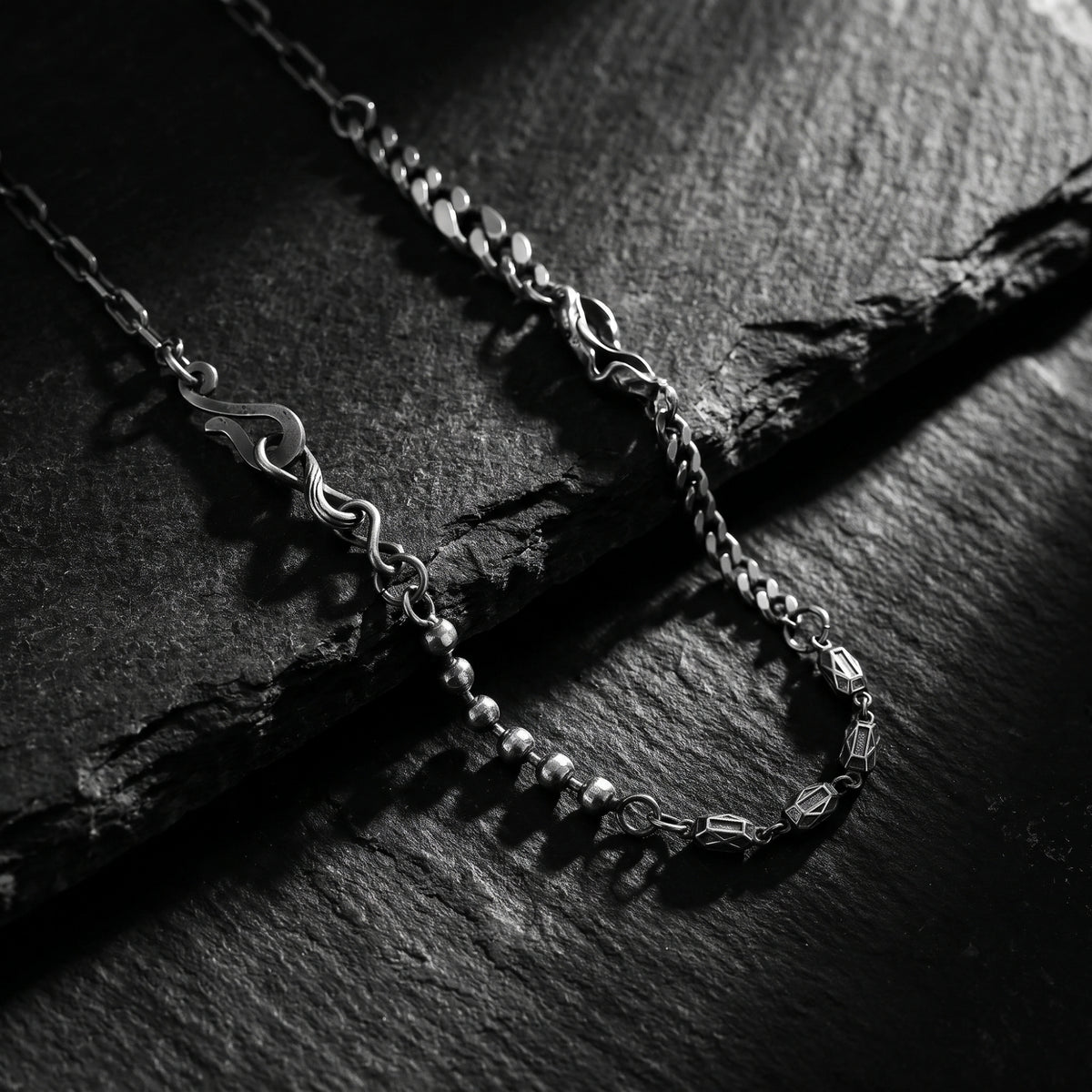 Close-up of the silver multi-link necklace resting on dark slate, showing round beads and geometric station links.